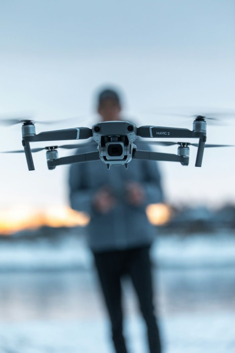 Close-up of inspection drone hovering with Shawn blurred in the background shown operating it.