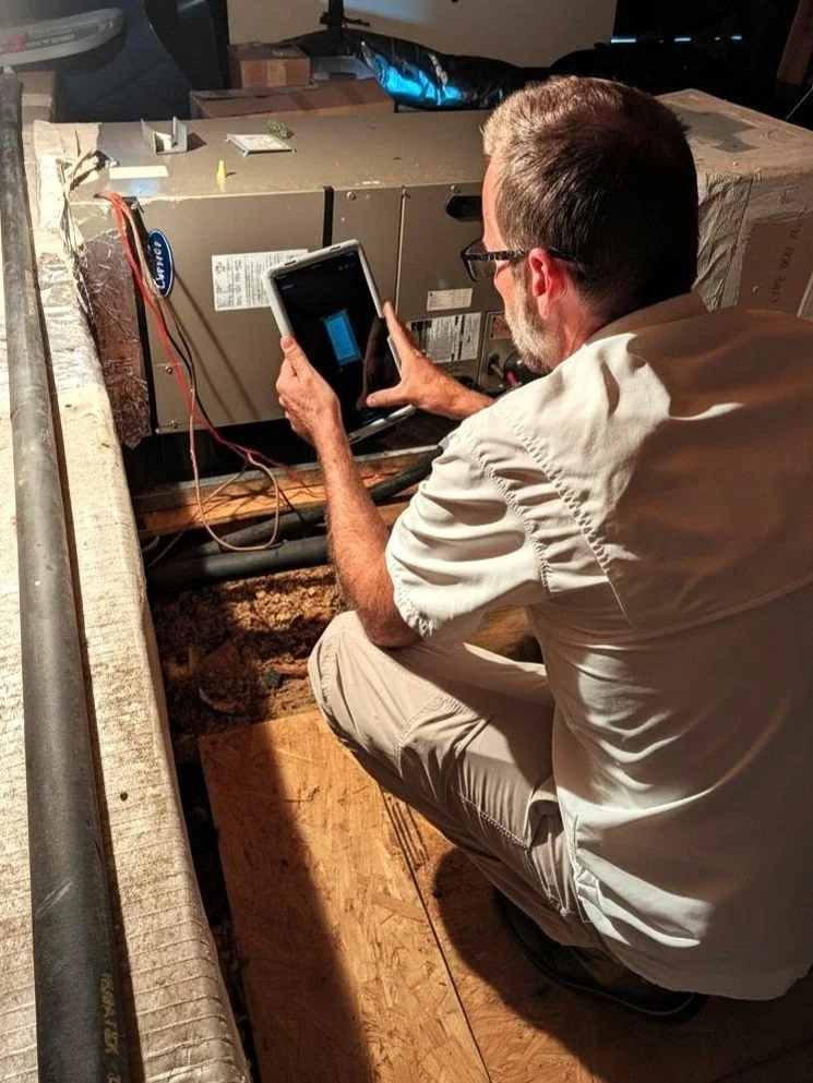 Inspector photographing attic air handler with tablet.