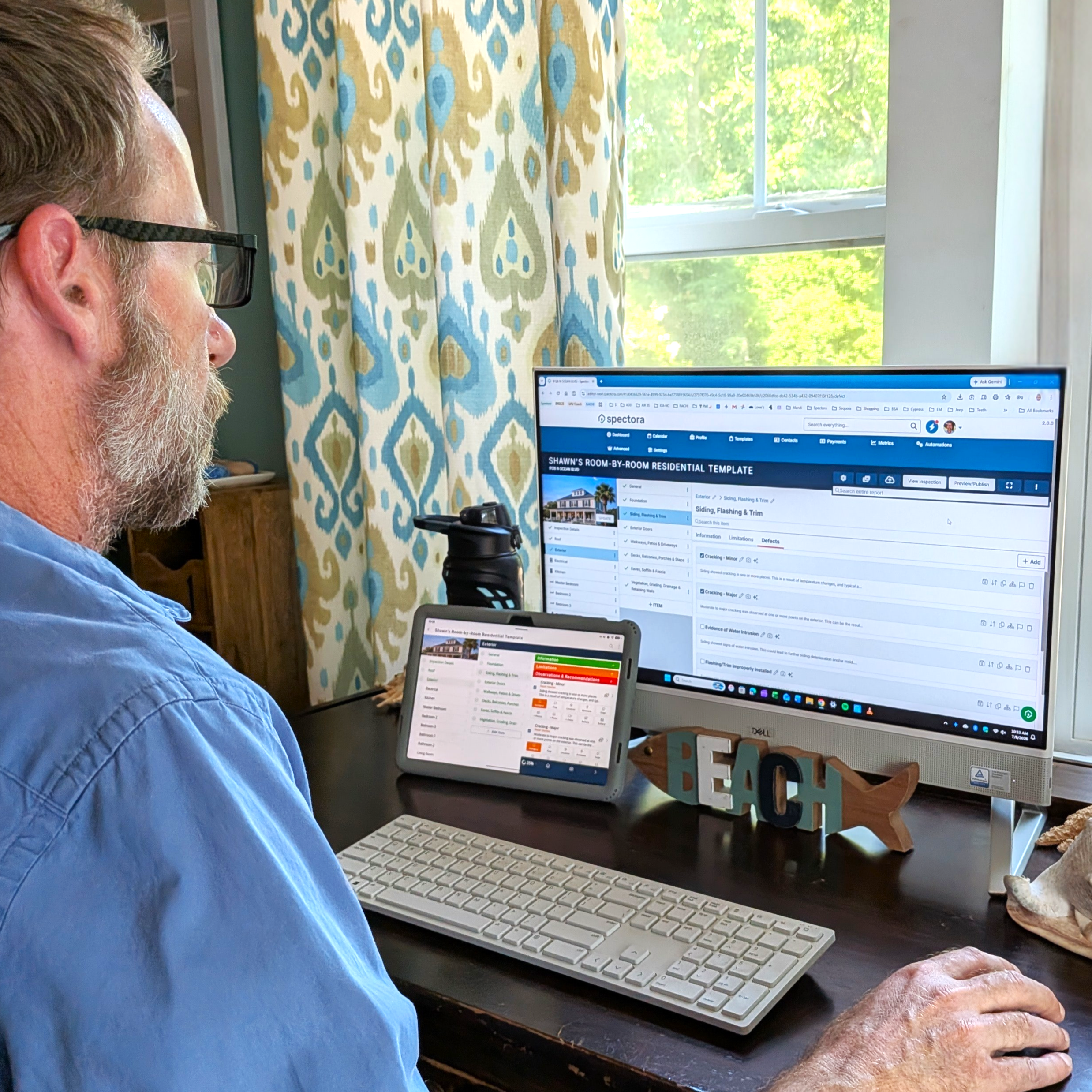 Home Inspector, Shawn DePenning, sitting at a desk reviewing and finalizing an inspection report on a tablet and desktop computer.