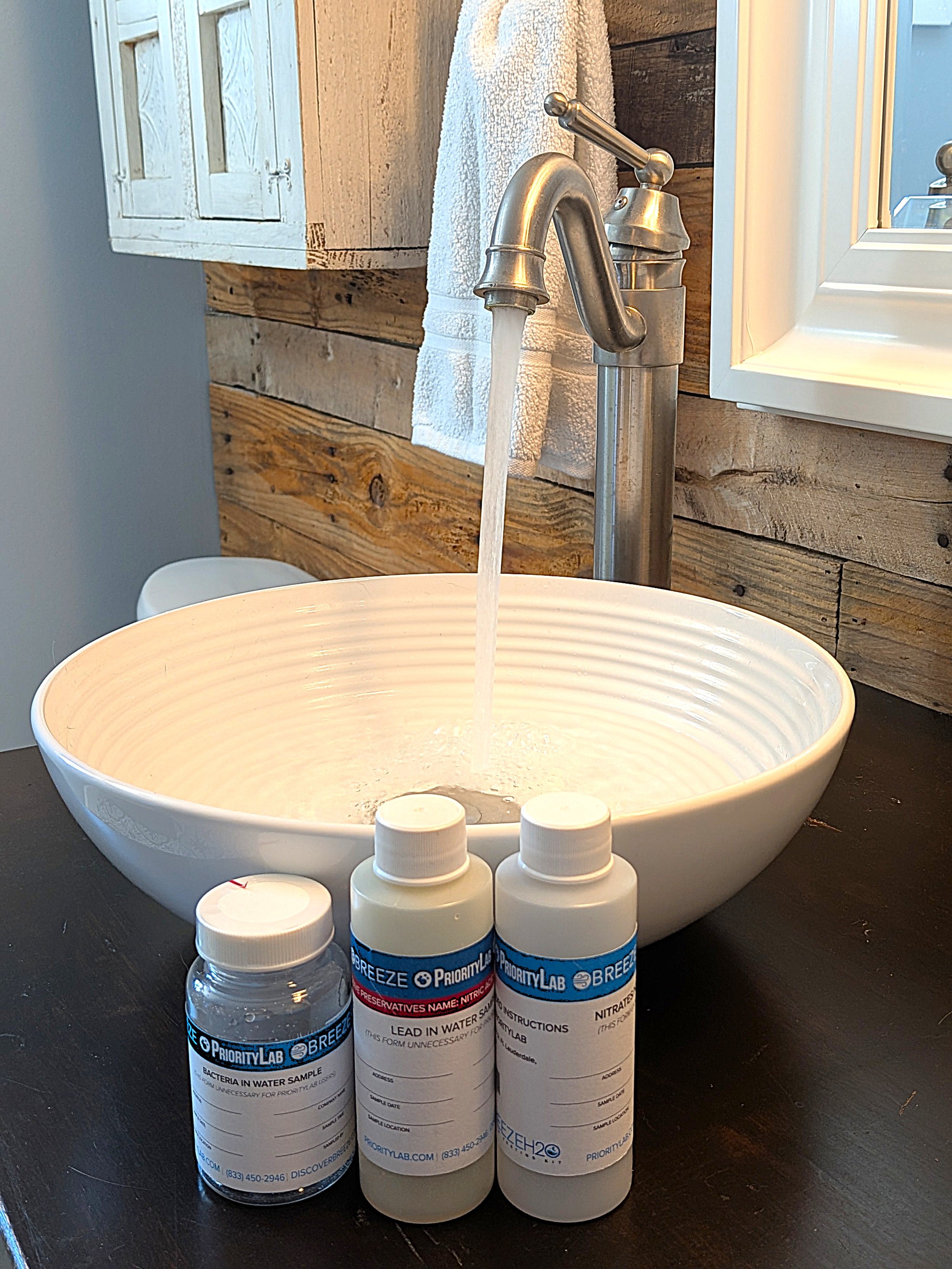 Water quality testing sample bottles on vanity in front of sink with faucet running.