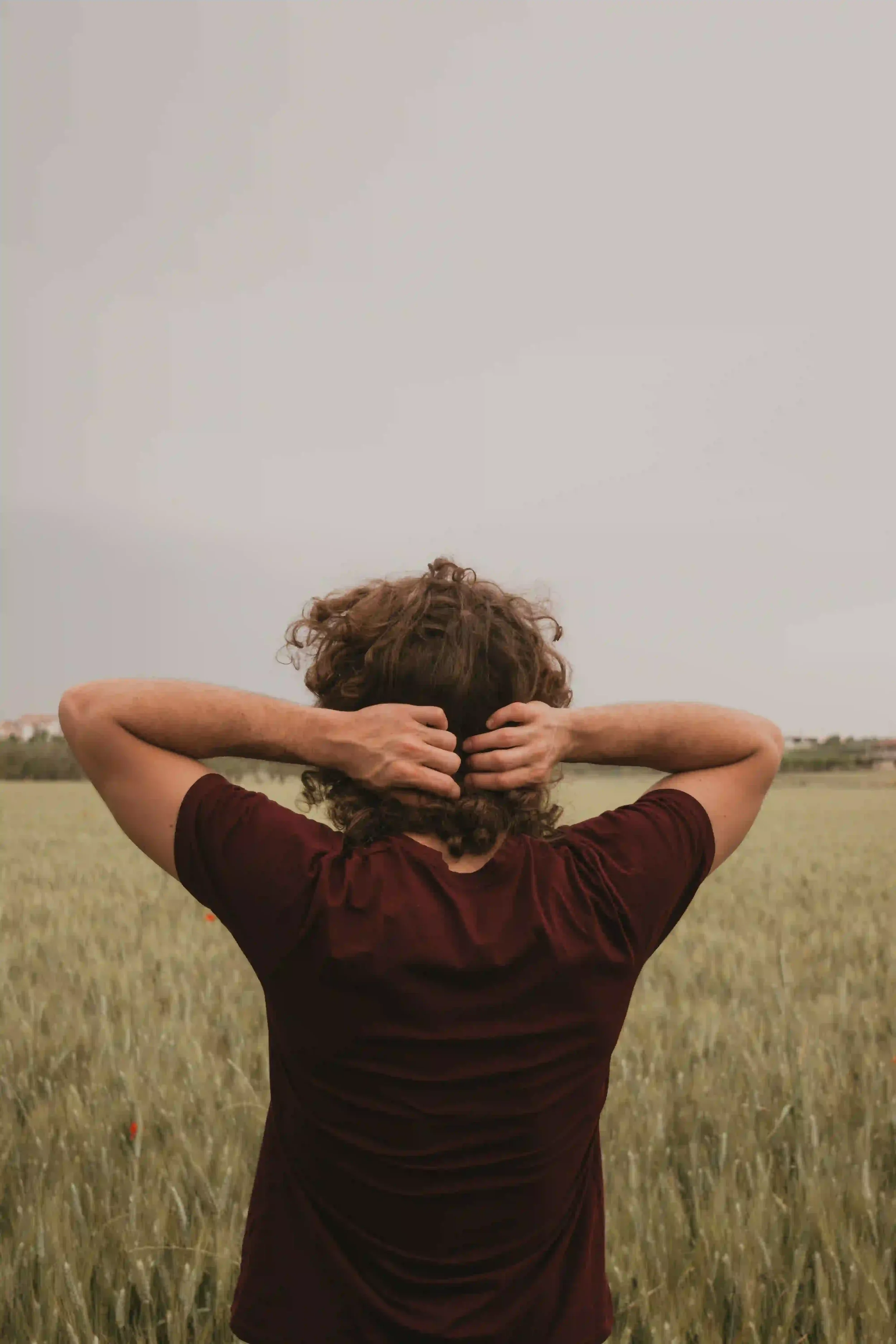Person standing in an open field with hands behind their head, suggesting trauma recovery, reflection, and emotional processing.