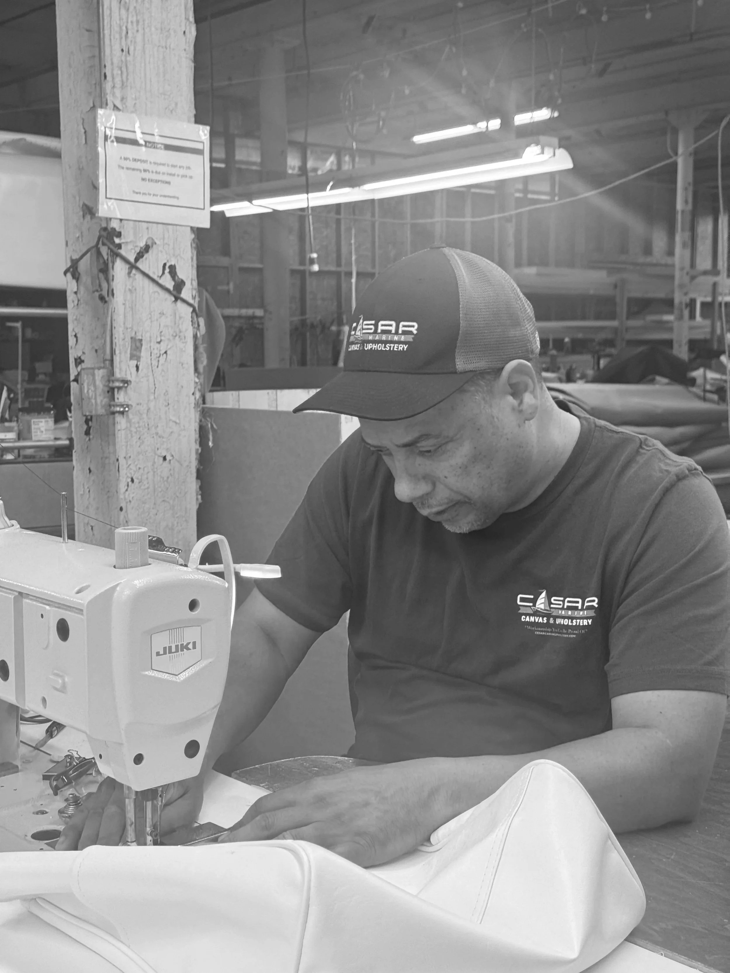 A man wearing a cap and T-shirt working on a sewing machine in a workshop.
