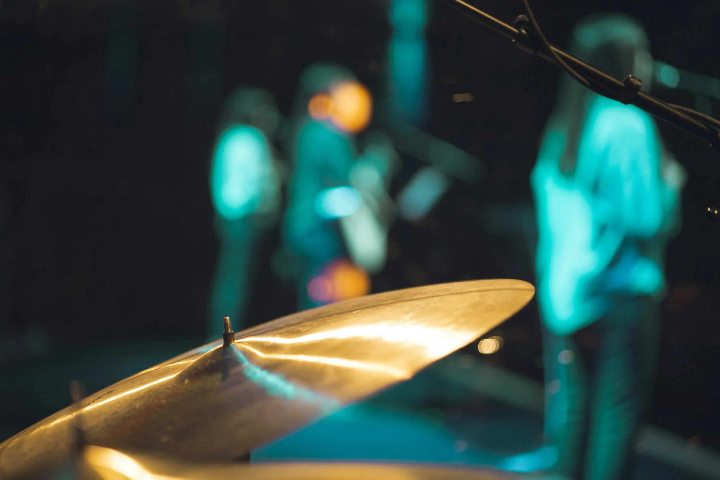 Close-up of a cymbal with a blurred background of glowing blue and orange lights, suggesting a concert or performance setting.