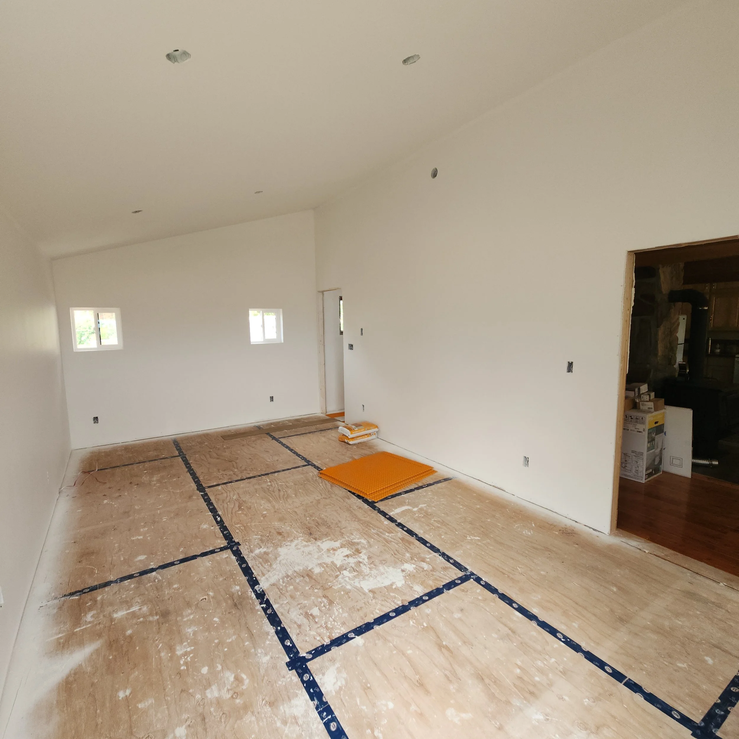 An unfinished room with drywall and taped joints, floor covered with protective paper, and some construction materials like foam tiles and boxes in the corner.