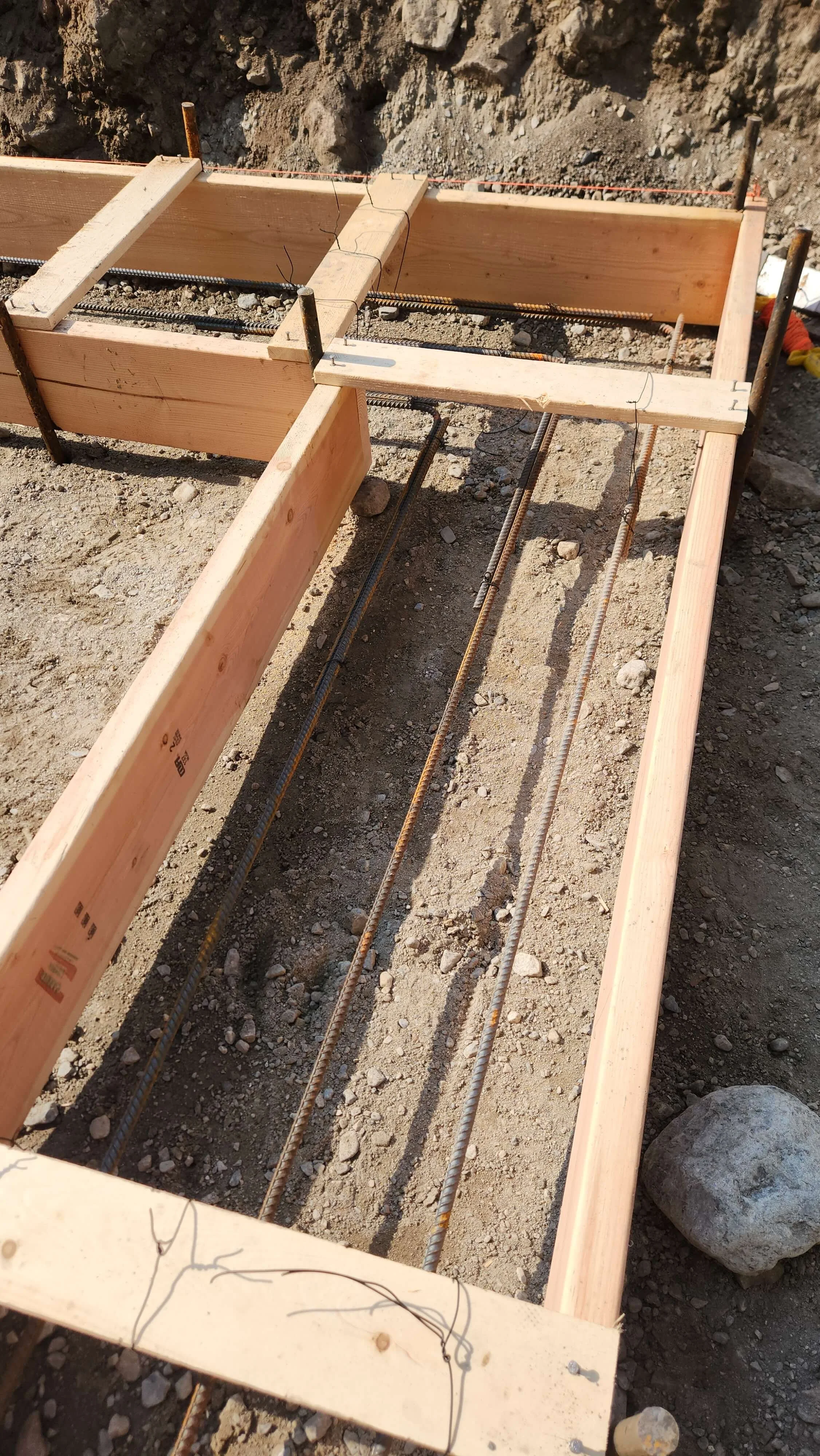 Wooden formwork for concrete with rebar and vertical support stakes on a construction site.