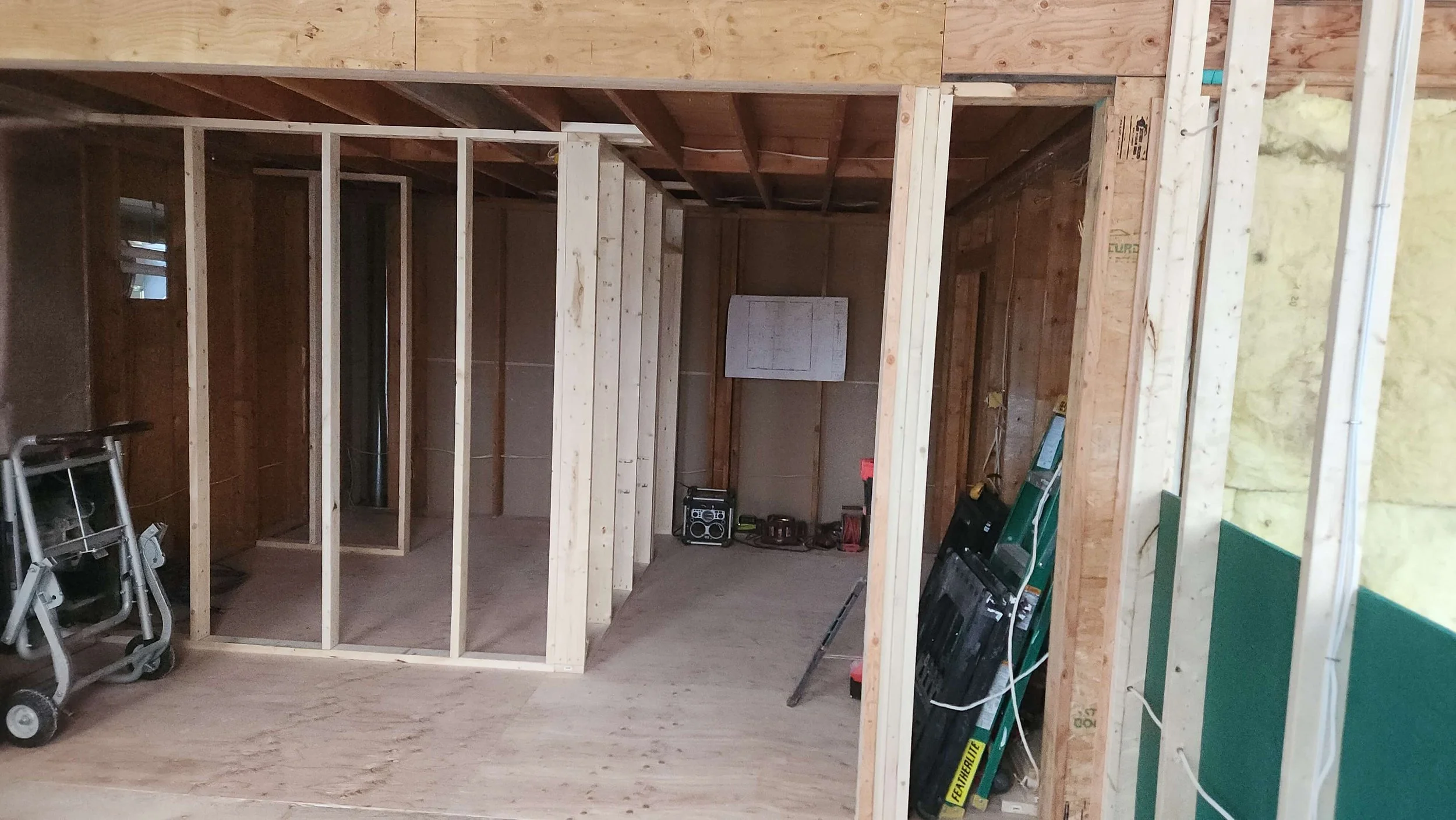 Interior of a house under construction with exposed wooden framing; tools and construction materials are visible.