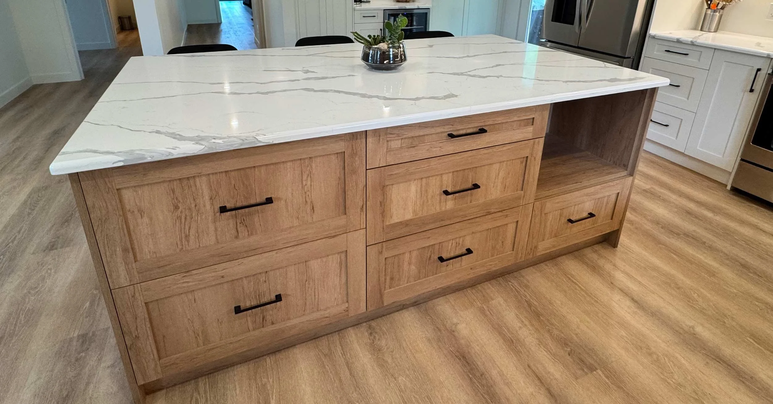 A kitchen island with a white marble countertop and wooden cabinetry with black handles, situated in a modern kitchen with white cabinets and stainless steel appliances.