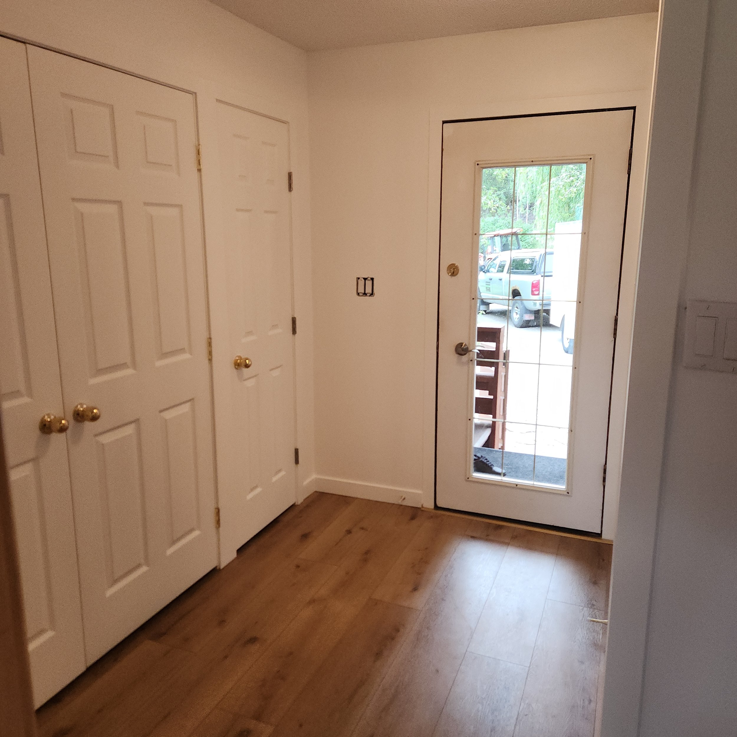 Entryway with a white tall closet, a window showing cars outside, and wooden flooring.