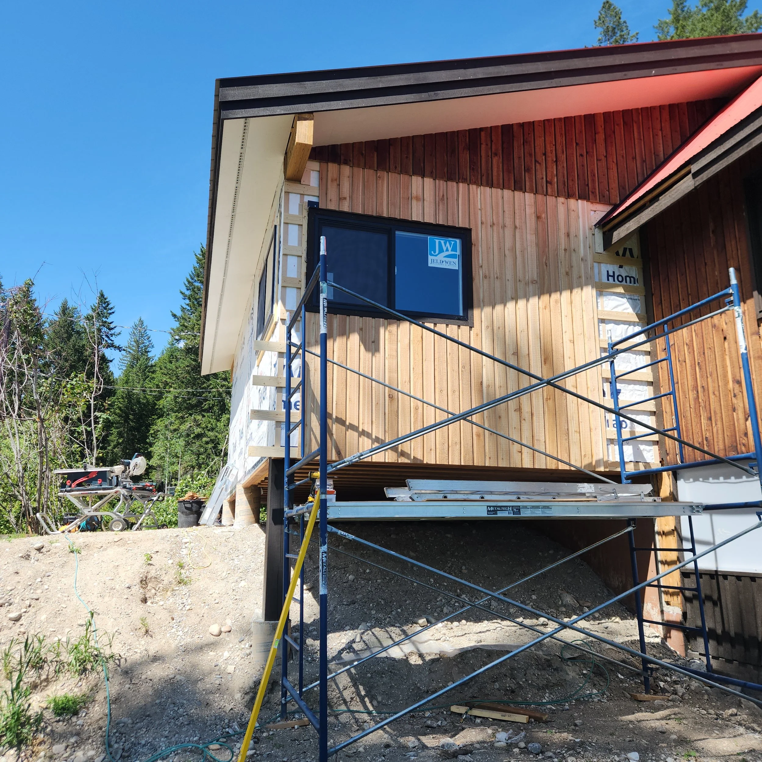 A house under construction with wooden exterior walls, a blue sky, and scaffolding in front.