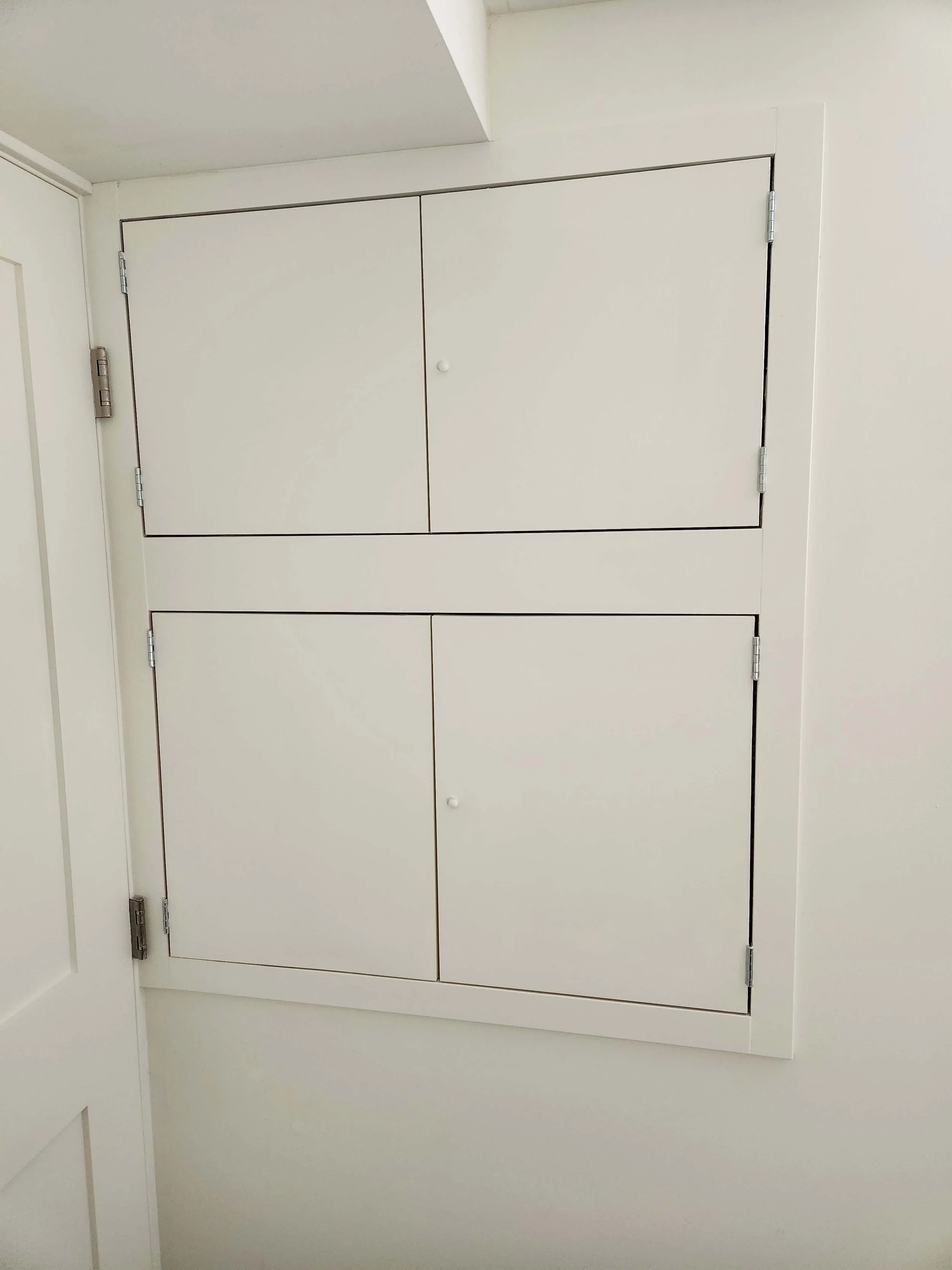 White cabinet with double doors, set into a white wall.