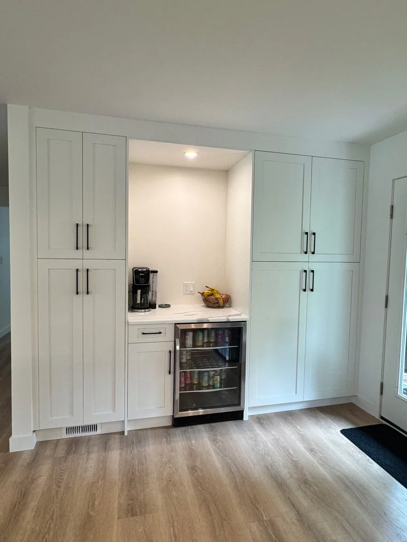 Kitchen corner with built-in cabinets, small beverage fridge, coffee maker, and a basket of bananas on the counter.