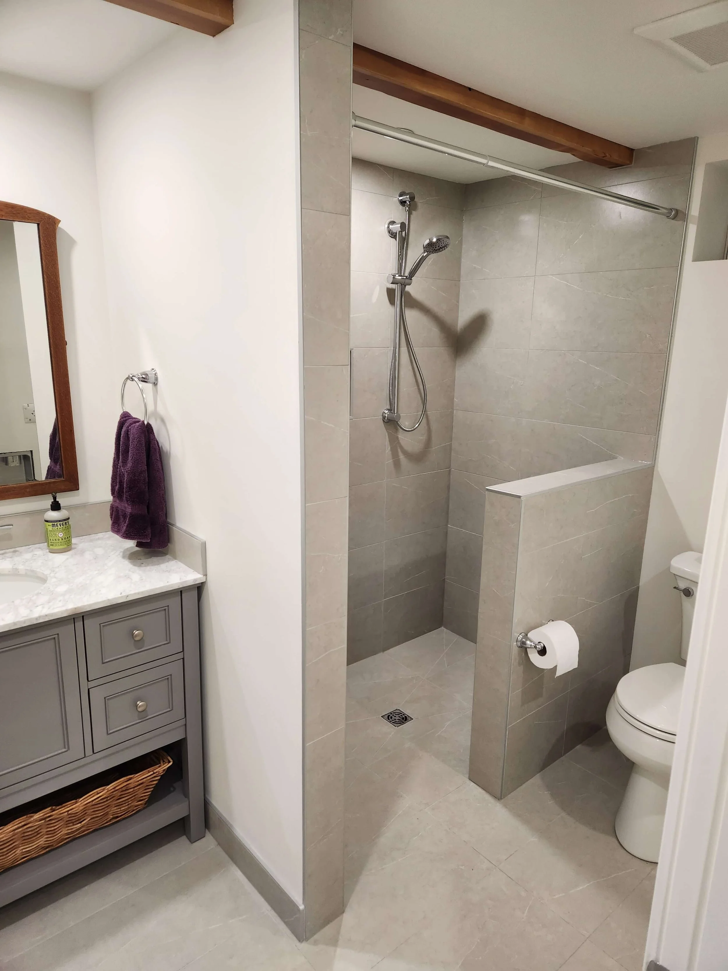 Bathroom with a walk-in shower, gray tiled walls, a toilet, a vanity with a gray cabinet, a purple towel on a ring, and a mirror.