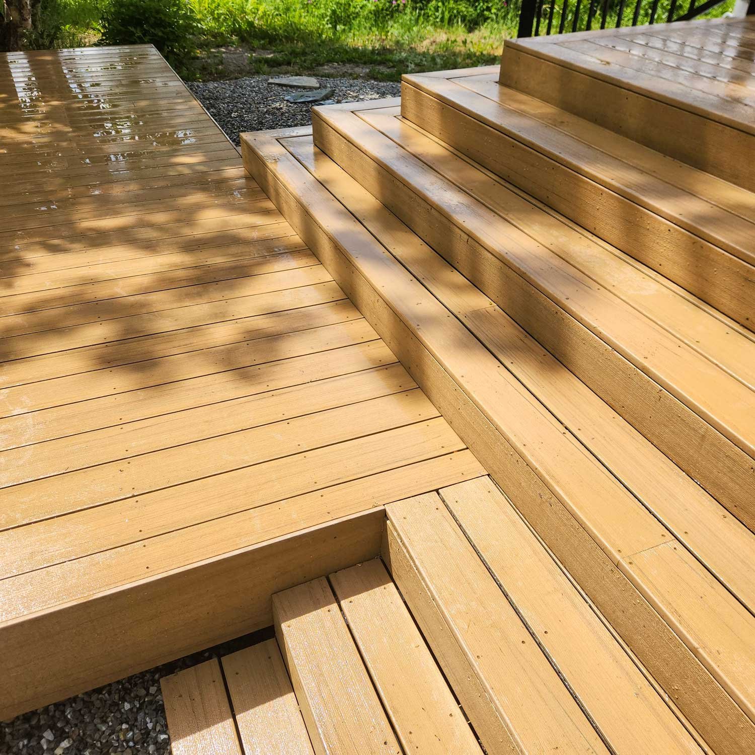 Wooden deck with steps leading to the grassy outdoor area, sunlight creating shadows on the surface.