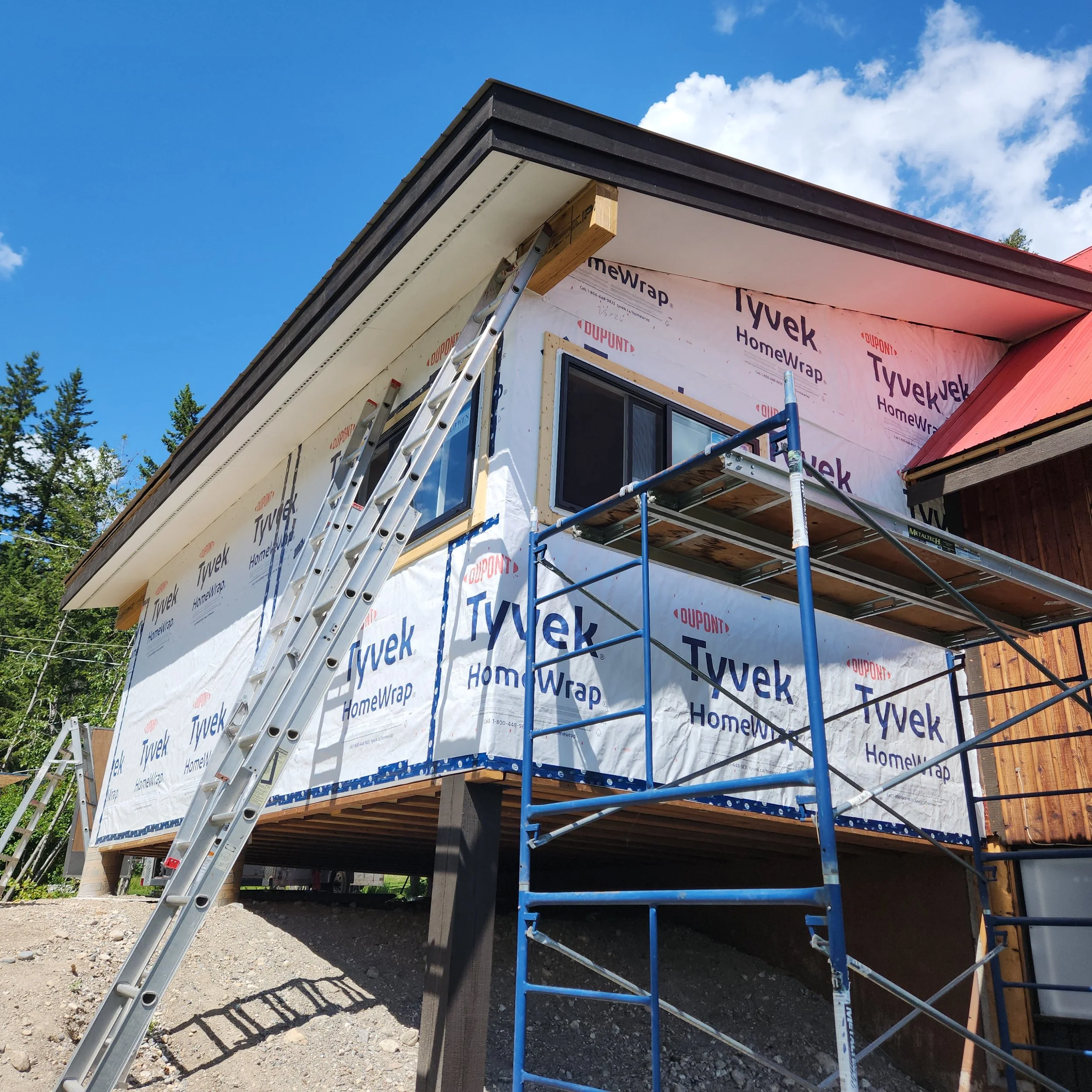 Construction site of a house with Tyvek HomeWrap and scaffolding, viewed from ground level under a clear blue sky.