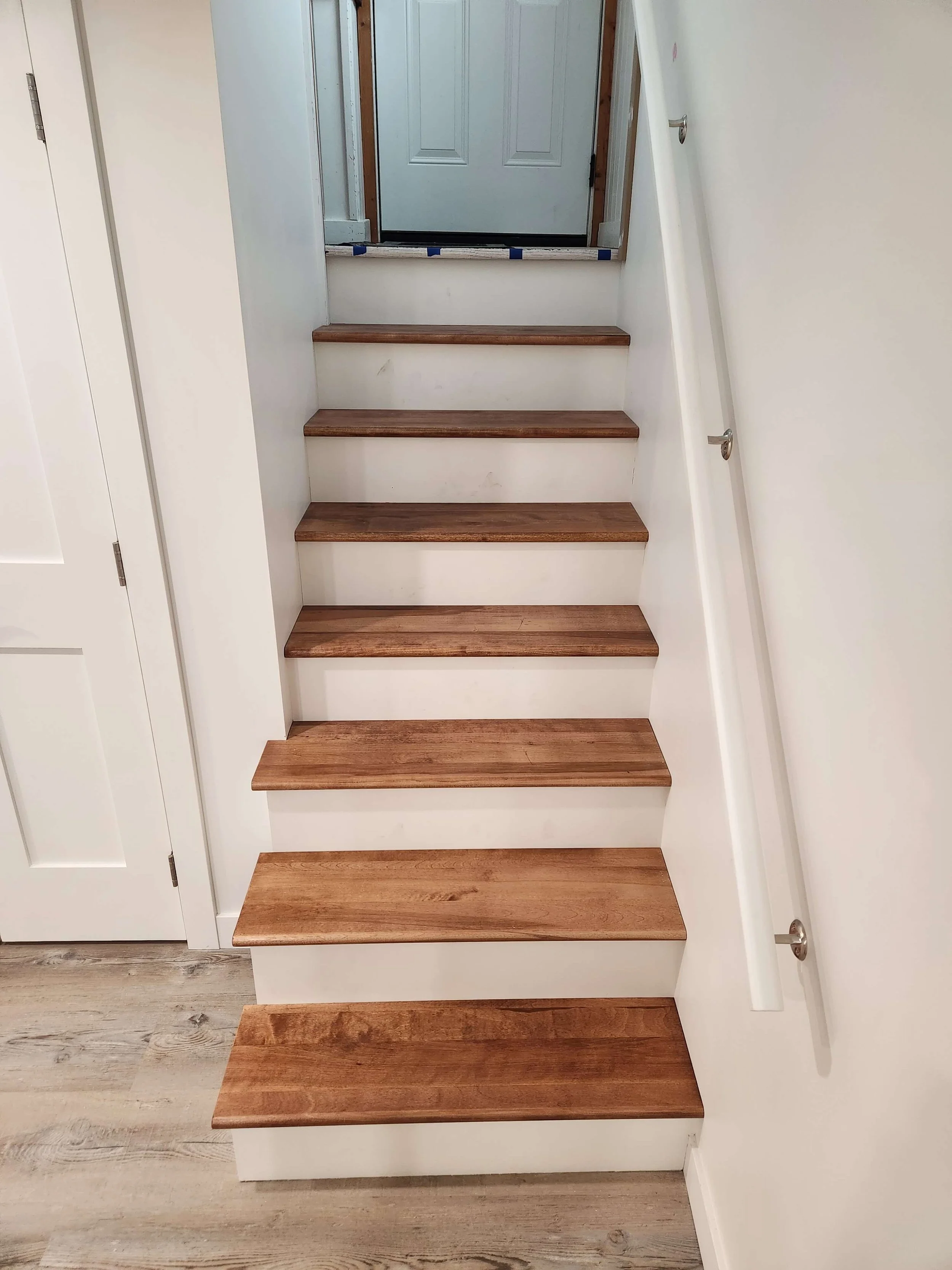 Wooden stairs with white walls and railing leading up to a door.