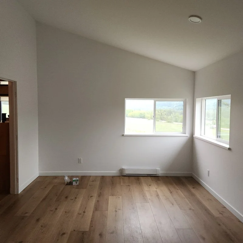 Empty room with white walls, hardwood floor, two windows, and a baseboard heater