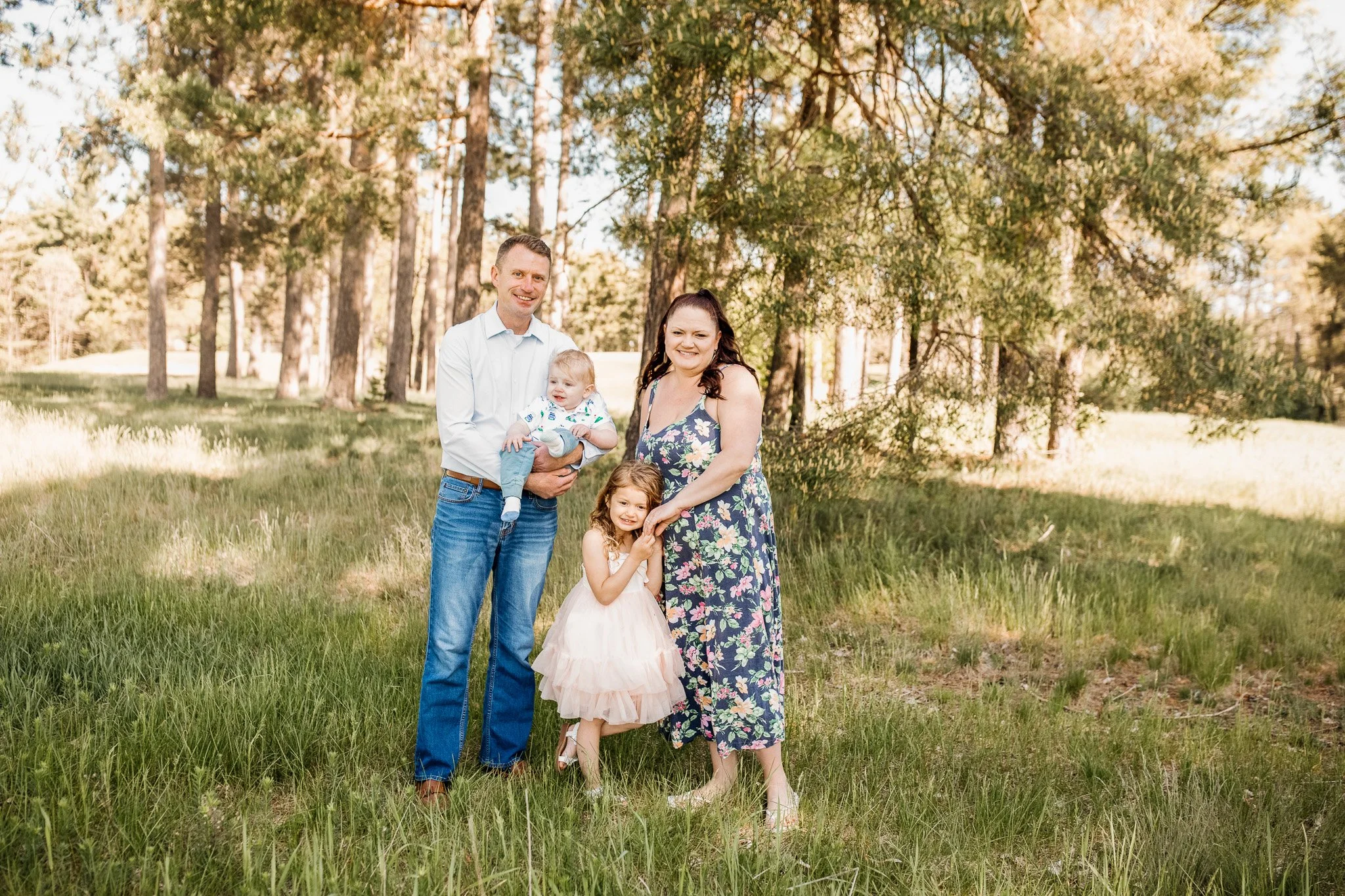 Brent Jacobson and his family in a grassy area with trees, including two adults, three children, and a baby, smiling at the camera.