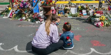 George Floyd memorial: A woman and a young girl sit at a memorial with flowers and tributes.