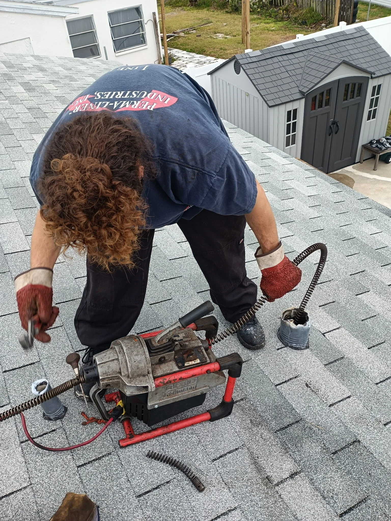 Team player kneeling on a rooftop, using a drain machine tool to clean the drain from the roof vent.