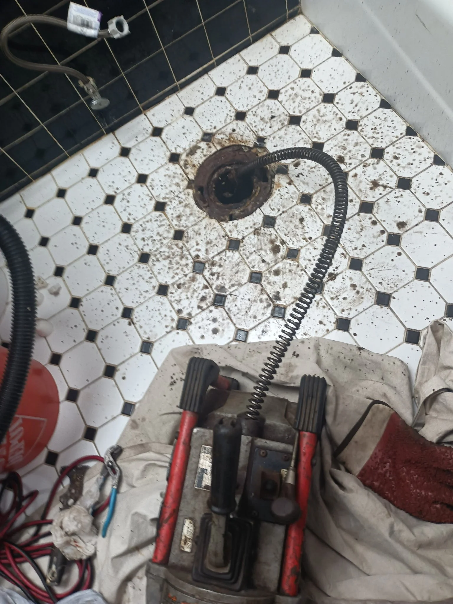Tools and equipment for plumbing or drain cleaning, with a focus on a drain and a pipe snake or auger. 