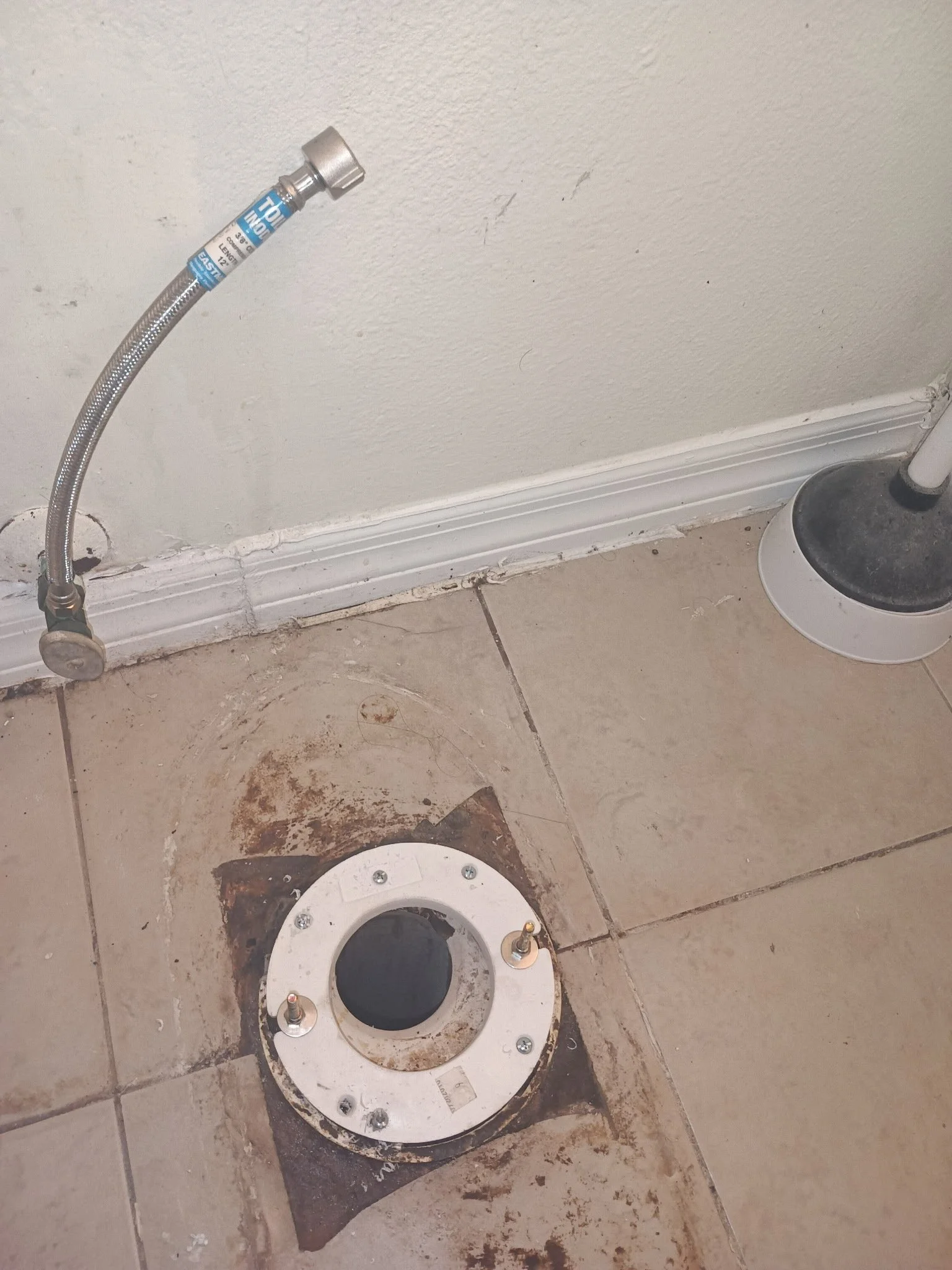 A bathroom floor with a toilet flange and a toilet base that has not yet been installed. The floor has some dirt and grime around the flange.