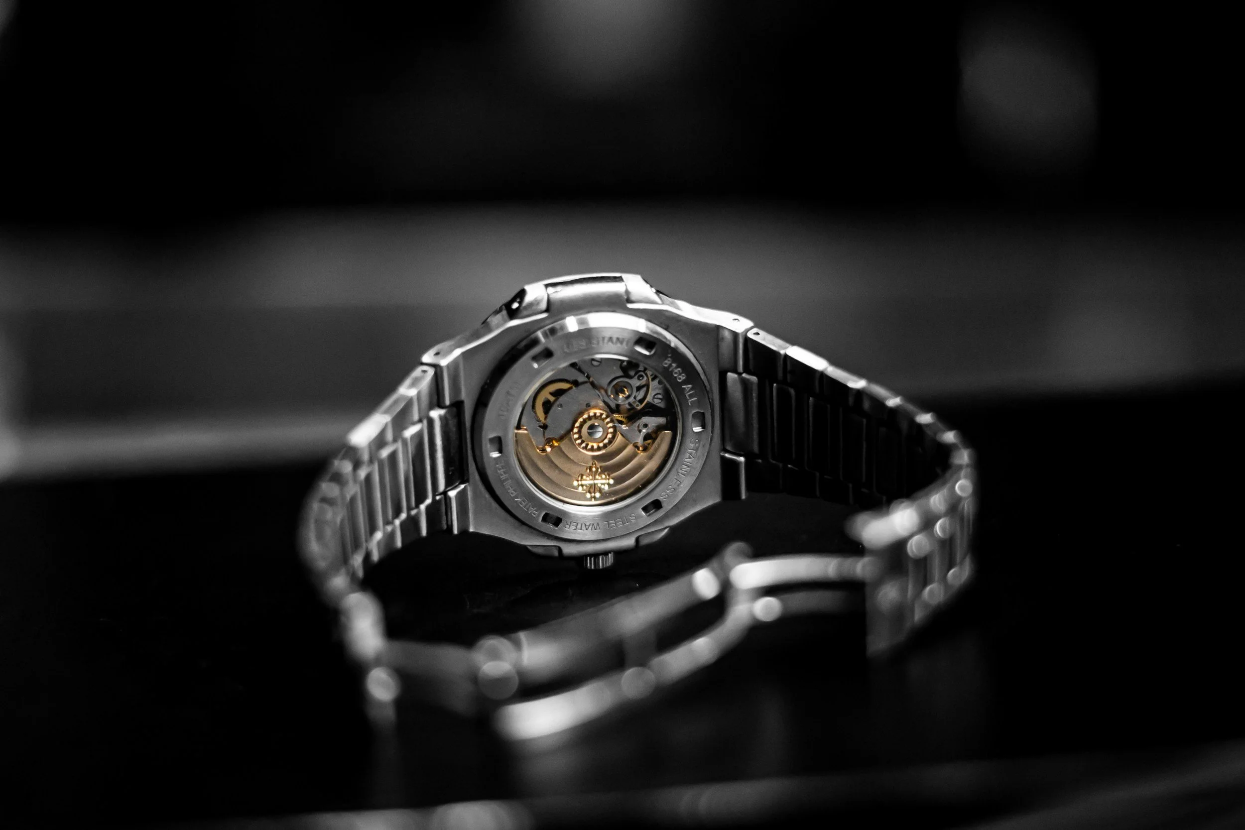 Close-up of a silver wristwatch with a visible mechanical movement, against a dark background.