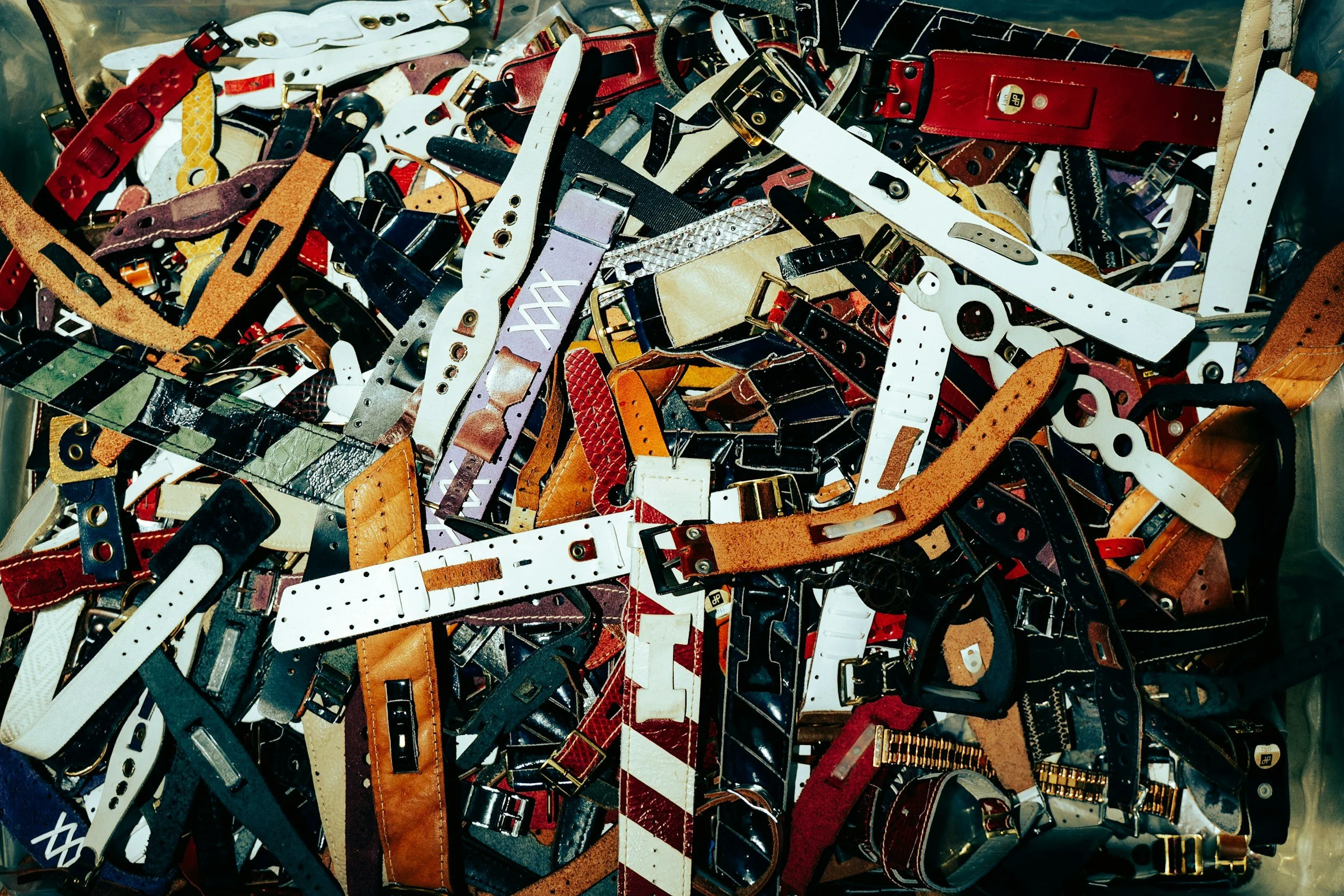 A large pile of assorted belts, mostly made of leather, with various colors, buckles, and styles.