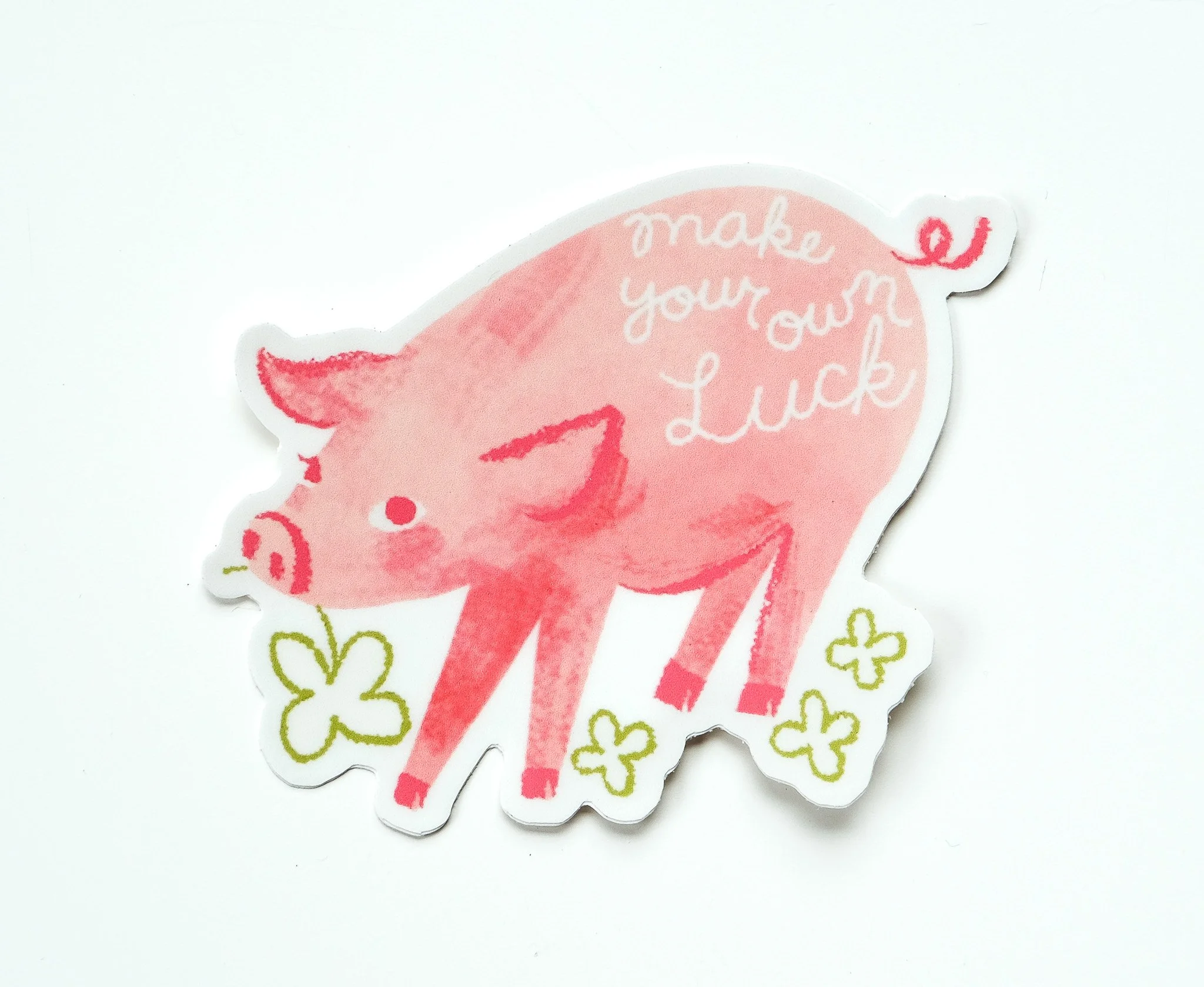 Pink sticker with a cartoon pig and the phrase "make your own luck" in white text, surrounded by green four-leaf clovers.