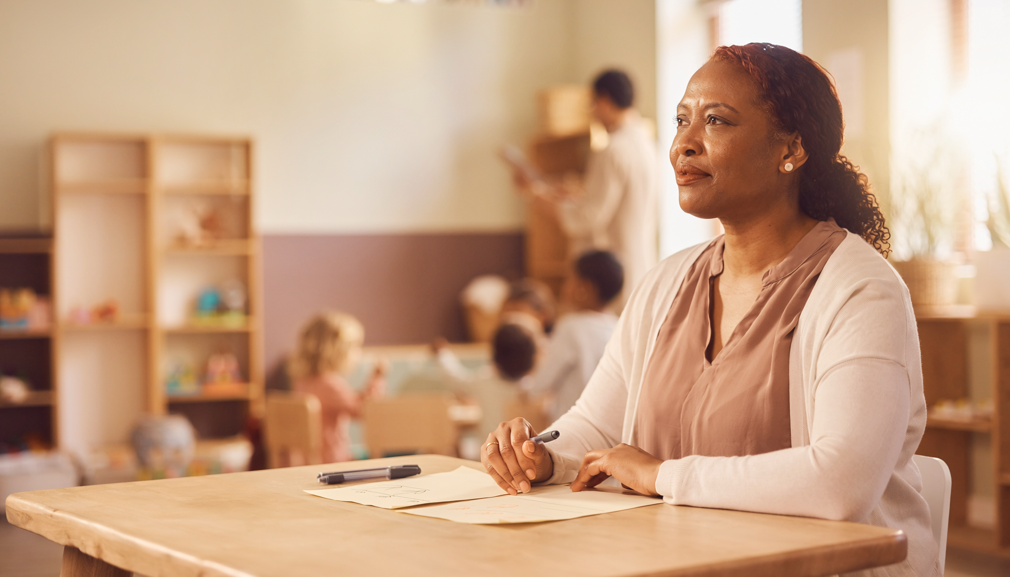 An early childhood program leader sits at a wooden table reviewing planning notes in a warm, natural-light workspace, reflecting on clarity, support, and leadership follow-through.