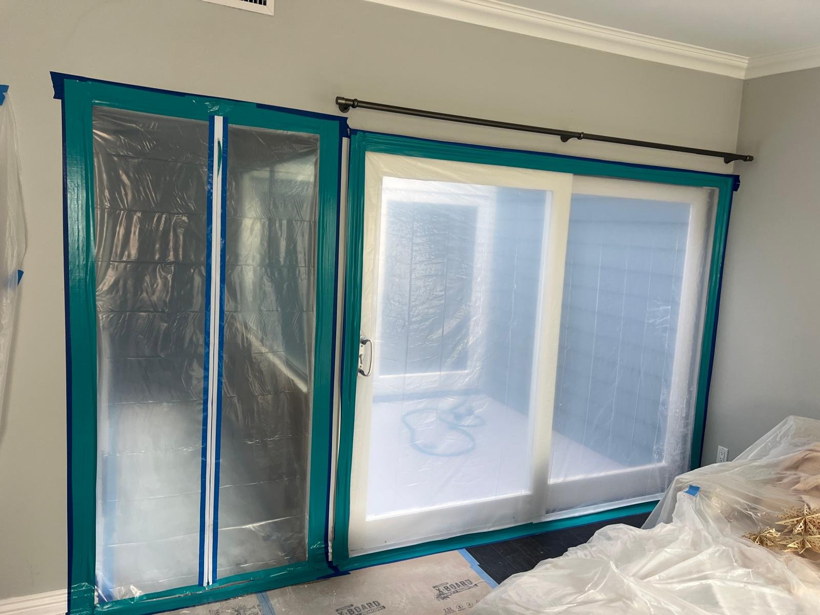Sliding glass door installation with protective plastic covering on the glass panels and blue painter's tape around the edges in an indoor room.