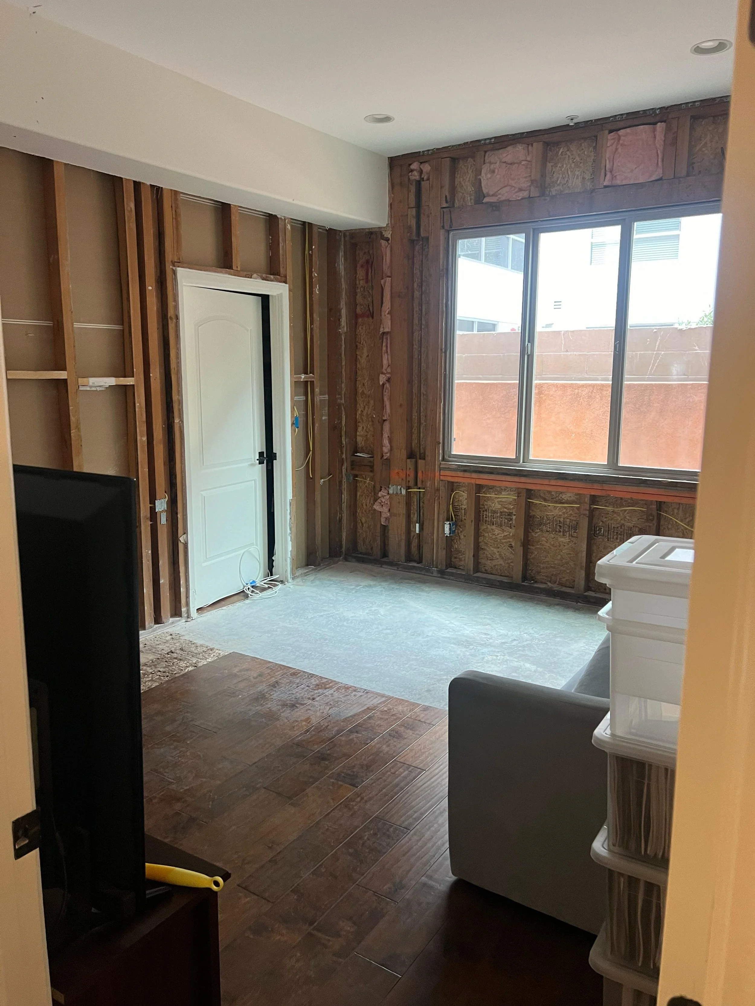 Interior of a room under renovation showing exposed wall studs, a sliding glass door, and a combination of completed and unfinished flooring.