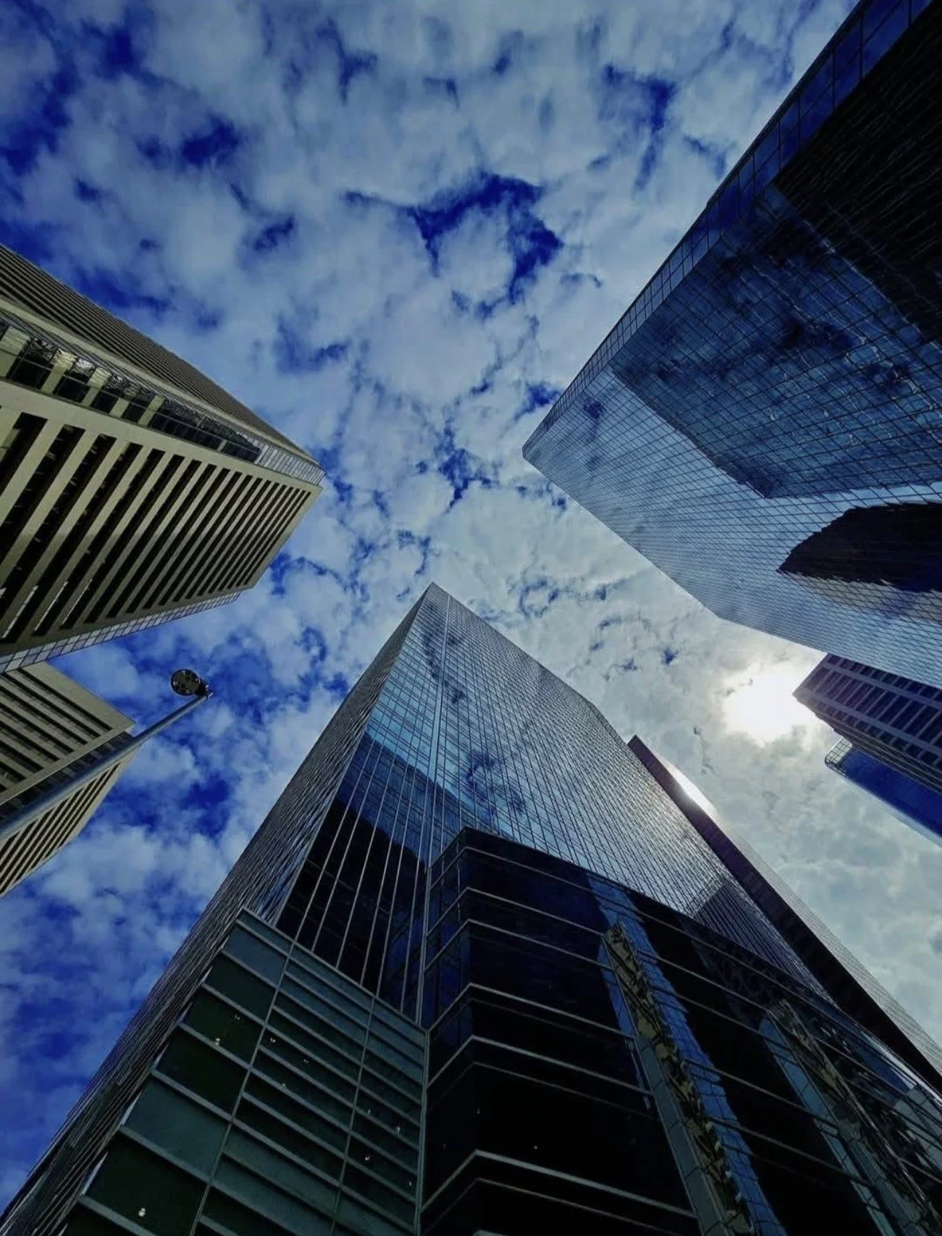 View of tall modern skyscrapers with reflective glass facades from a low-angle perspective, under a partly cloudy sky.