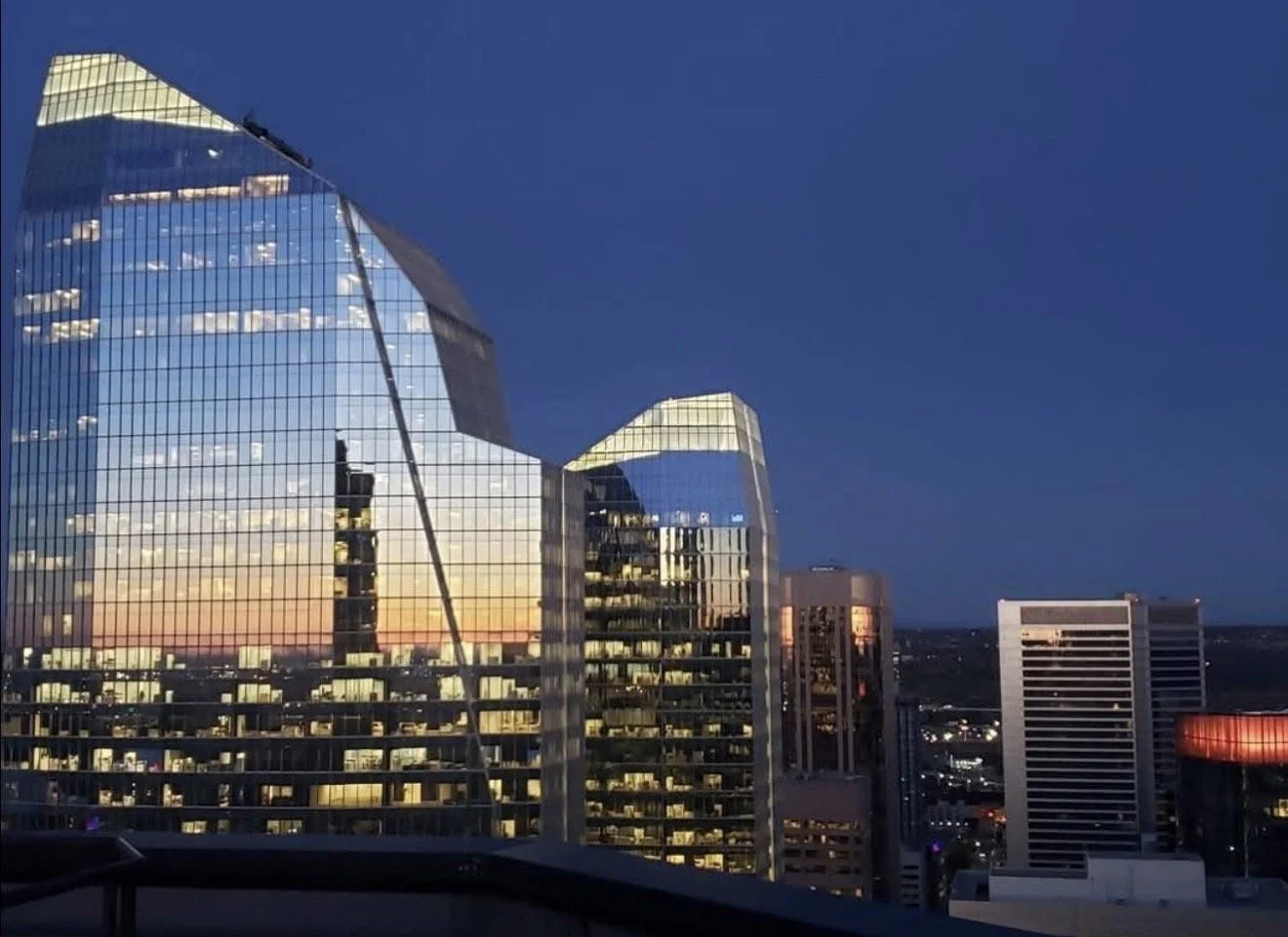 City skyline at dusk featuring modern glass skyscrapers reflecting the evening sky, with a clear deep blue sky in the background.
