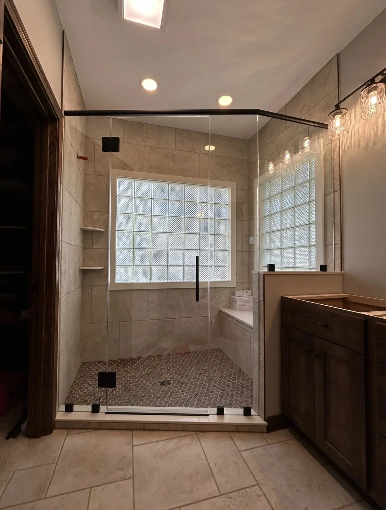 Bathroom with a glass-enclosed shower, beige tile walls, a window with glass blocks, wooden cabinets, and vanity lighting.