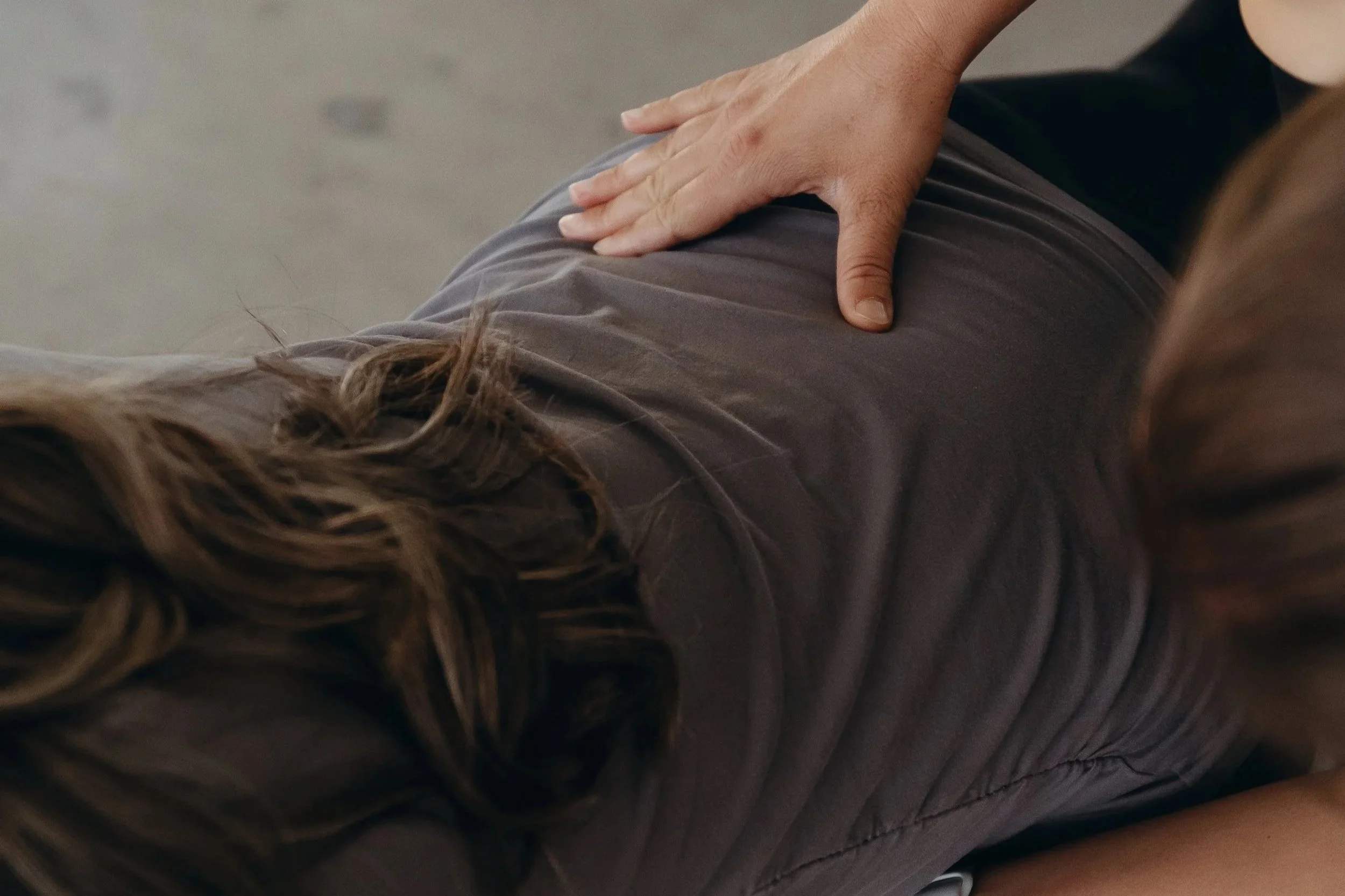 A person wearing a black top, palpating the back of a woman wearing a grey shirt.