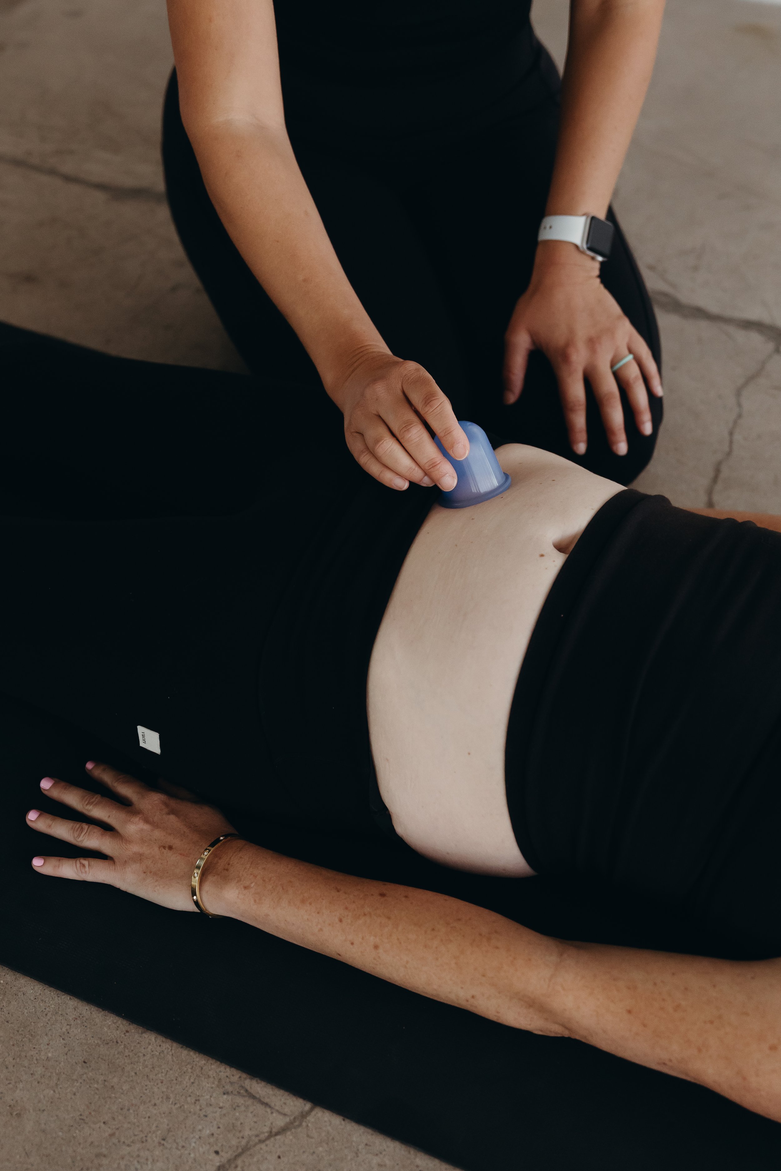 Person performing cupping therapy on another person's c-section scar, while seated and wearing black clothes and a smartwatch.