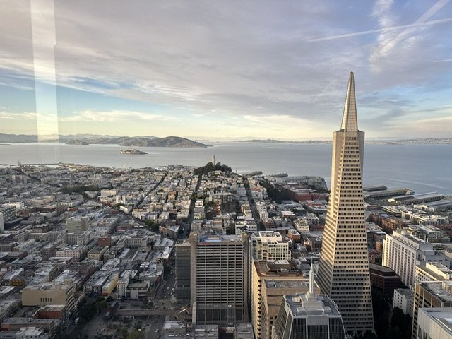 Aerial view of San Francisco skyline with the Transamerica Pyramid and waterfront, partly sunny and cloudy sky.