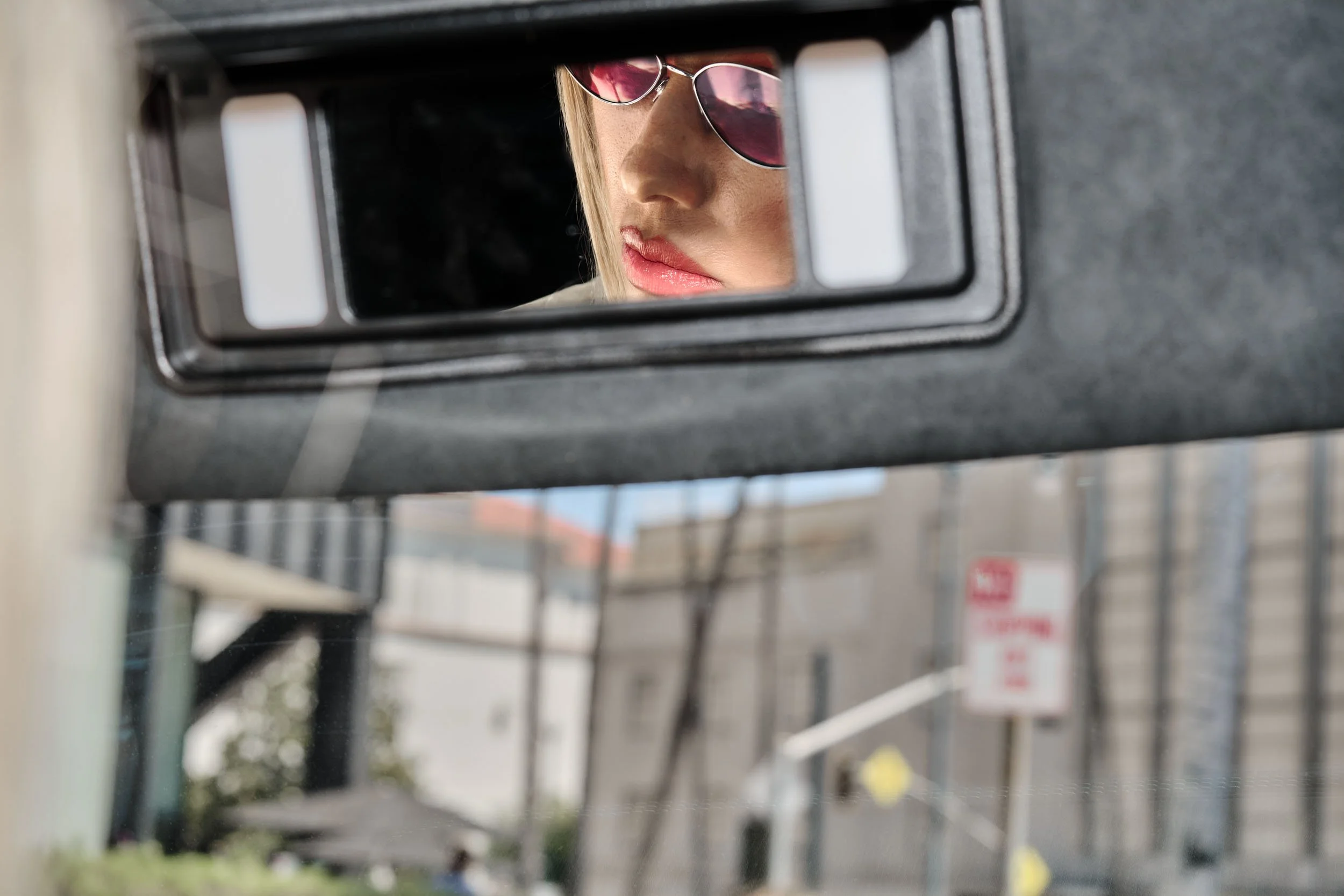 Reflected image of a person wearing red sunglasses, viewed through a security mirror, outdoors with trees and buildings in the background.