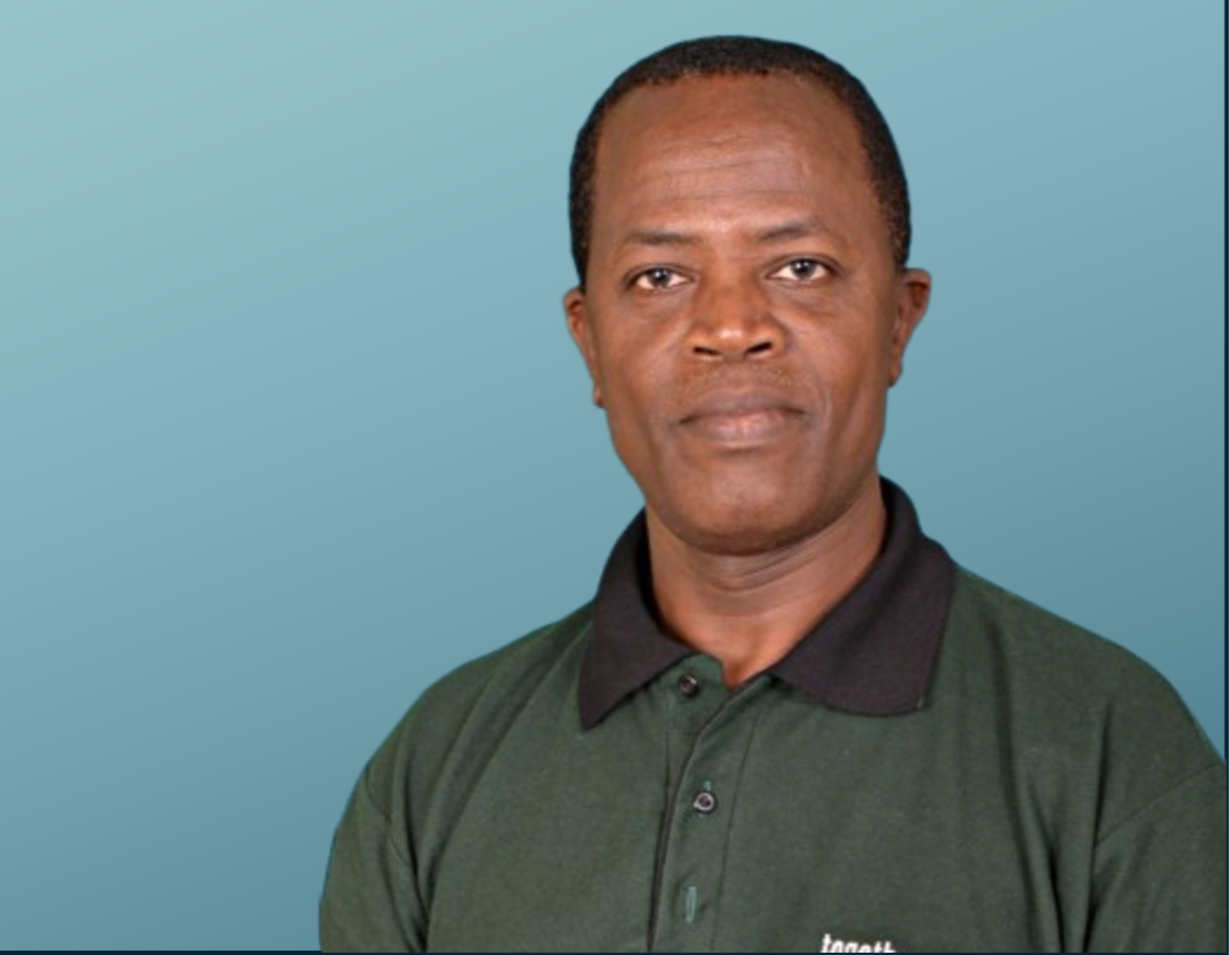A man with short black hair, wearing a dark green collared shirt and dark blazer, standing against a light blue background.