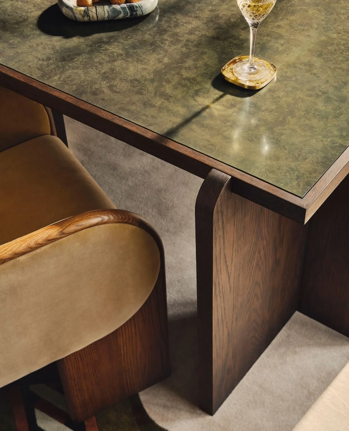 Warm modern dining table with a green marble top and upholstered chair in golden light.