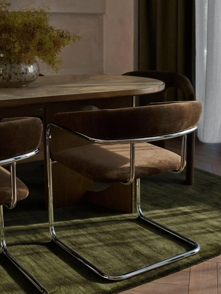 Warm modern interior with an upholstered chair, wooden table, and window light.