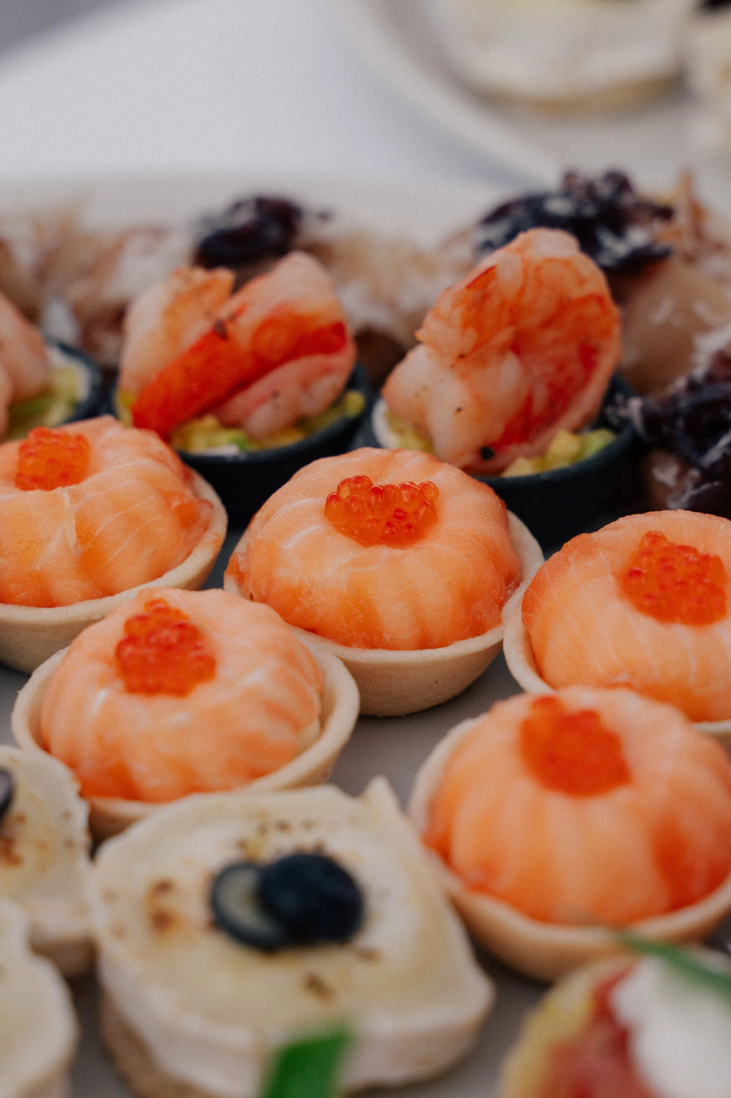 Assorted small appetizers including smoked salmon with orange fish roe, shrimp in pastry cups, and crackers with toppings.