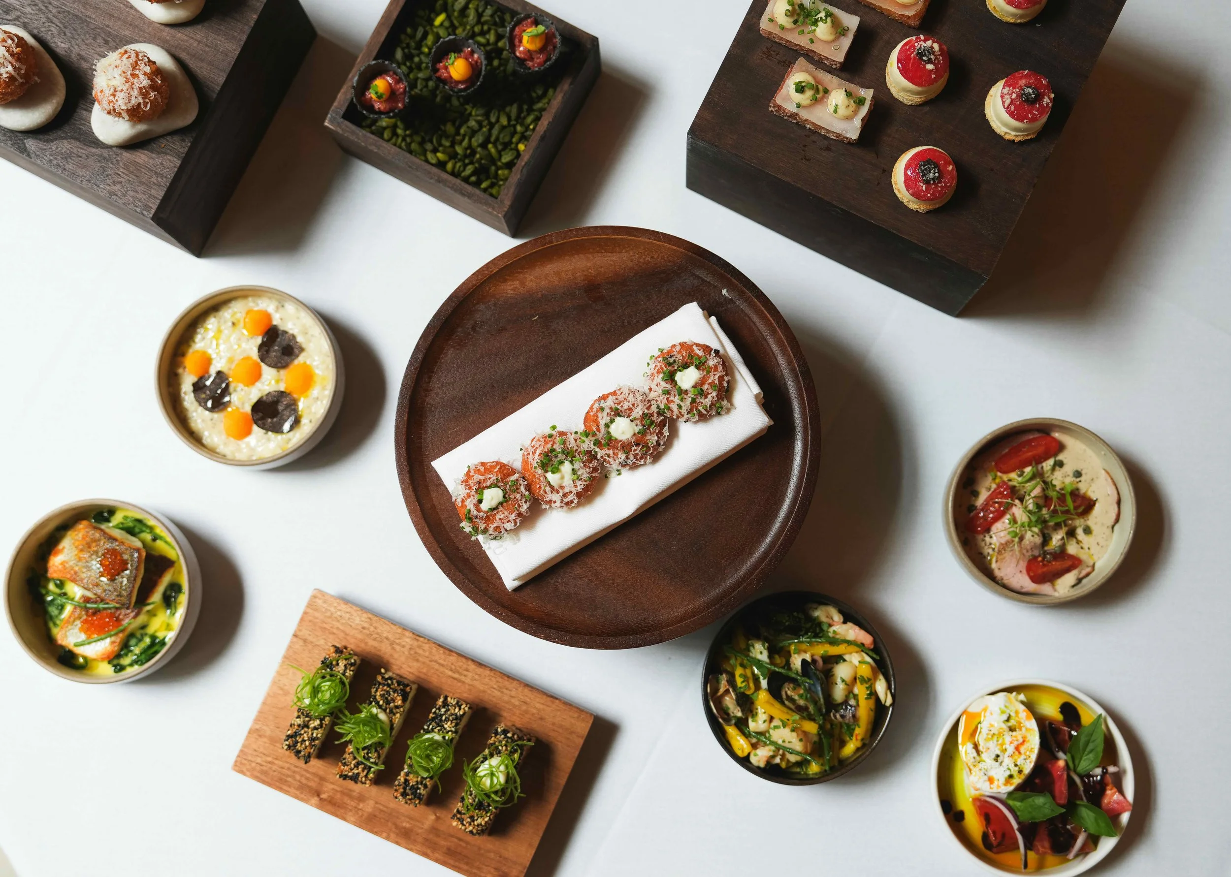 Assorted small gourmet dishes including bites, canapés, and appetizers arranged on wooden and ceramic platters.