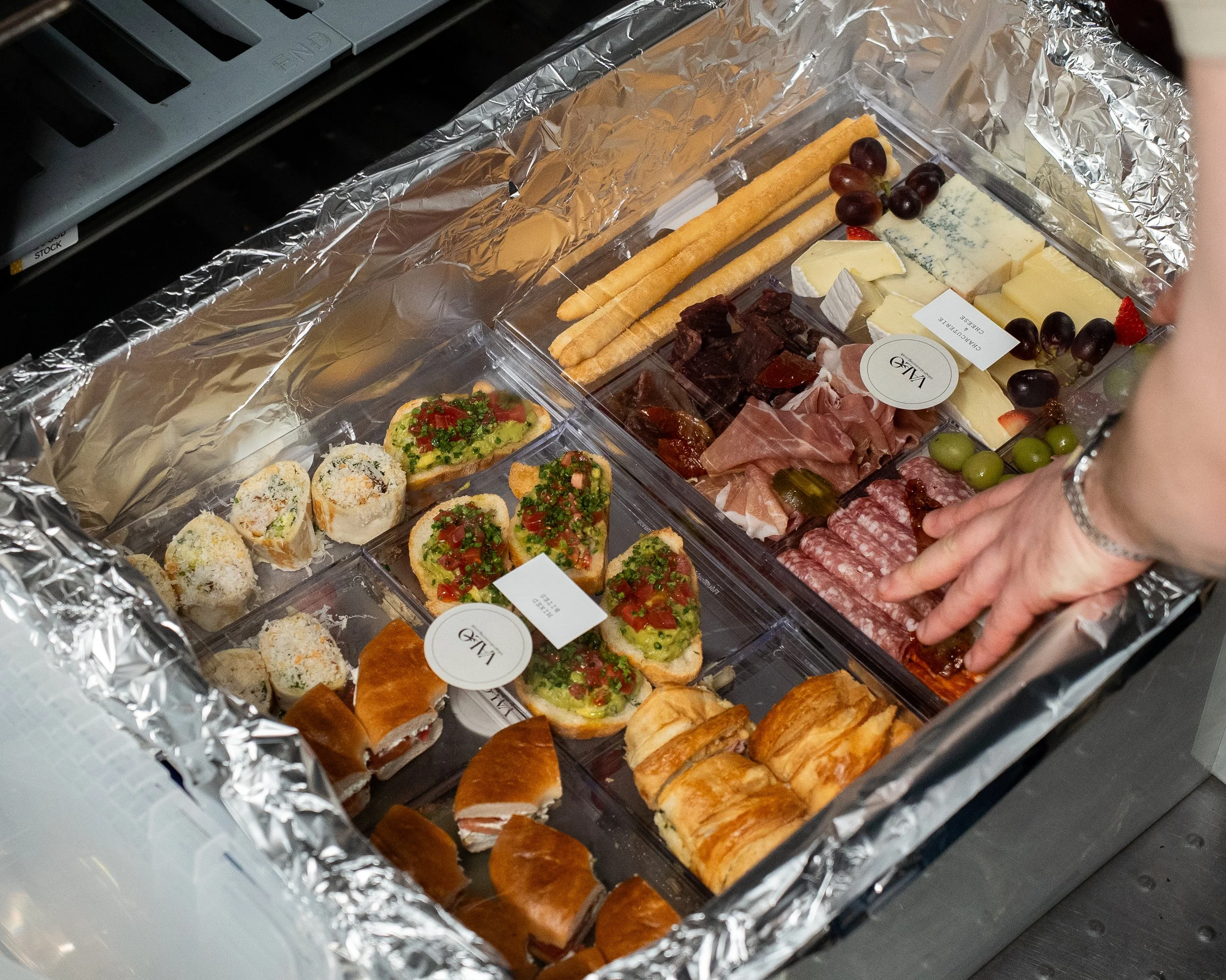 A tray of assorted cheeses, grapes, crackers, and cured meats inside a foil-lined container.
