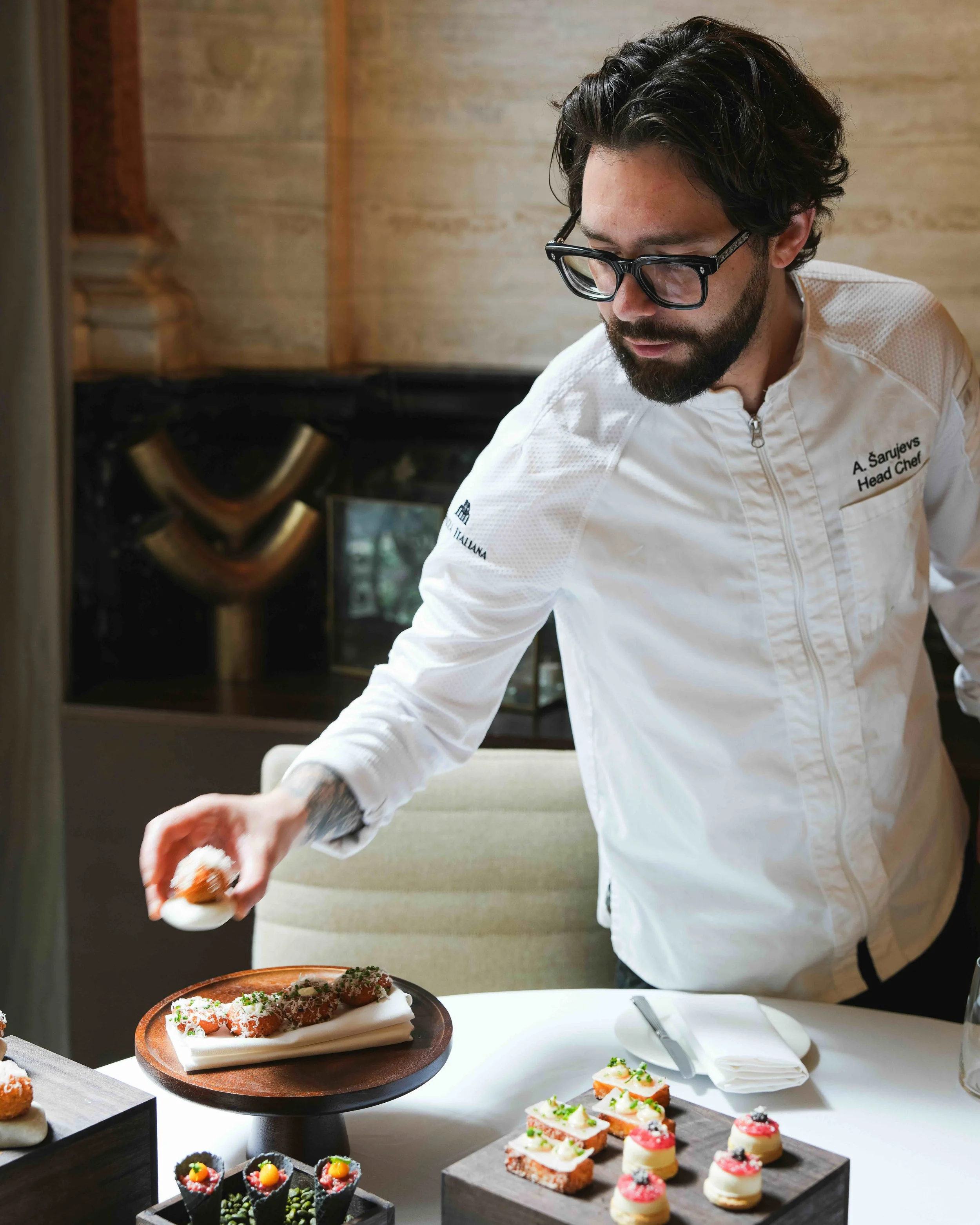 A chef placing food on a white plate at a table with various elaborately decorated desserts and appetizers.