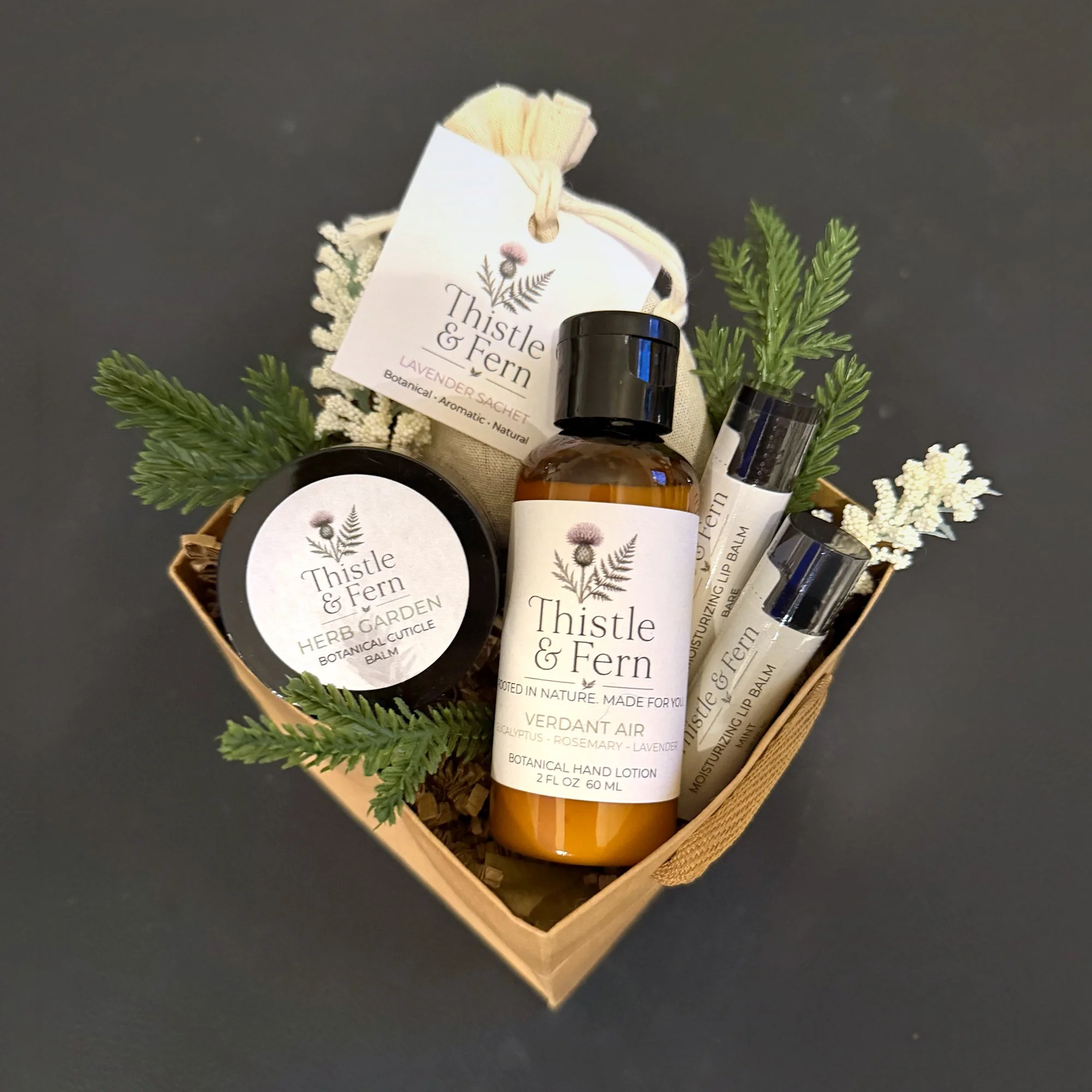 Thistle & Fern Stocking Stuffer Gift Basket with a 2 oz Botanical Hand Lotion, two lip balms, a Botanical Cuticle Balm and a Lavender Botanical Sachet in a kraft basket with evergreen sprigs