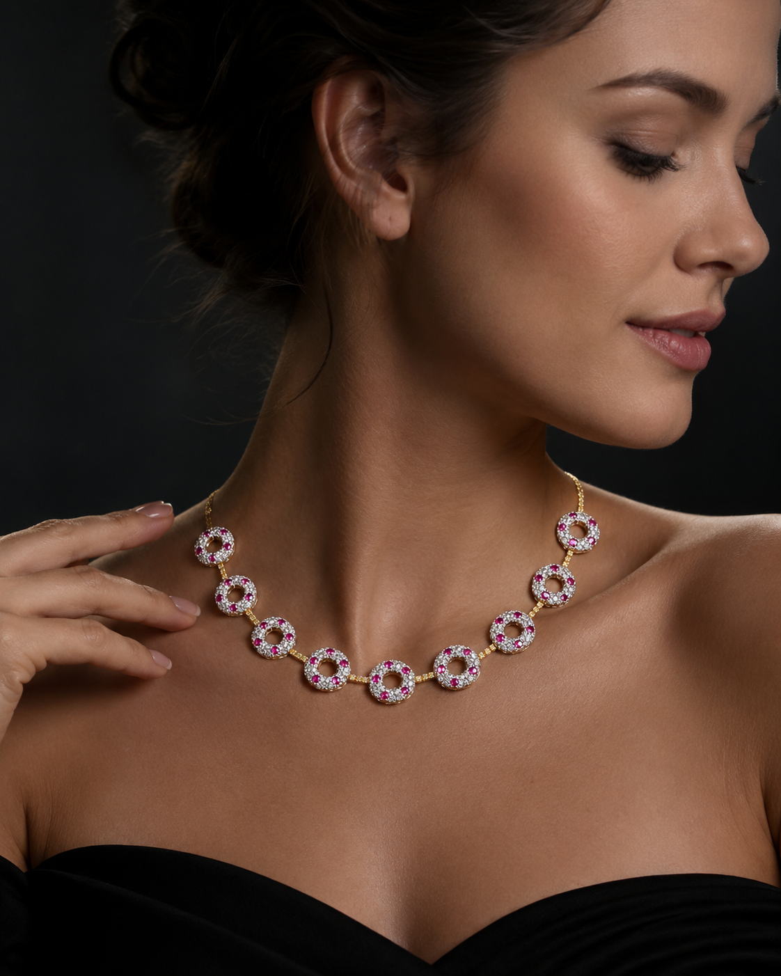 A woman is wearing a gold necklace with circular, pink, and white gemstones, with her eyes closed and her hand gently touching the necklace.