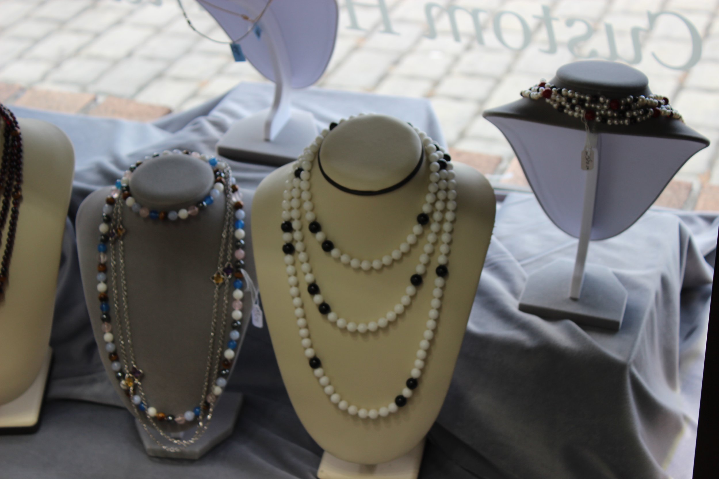 Display of various pearl and bead necklaces on jewelry busts at a craft fair or shop.