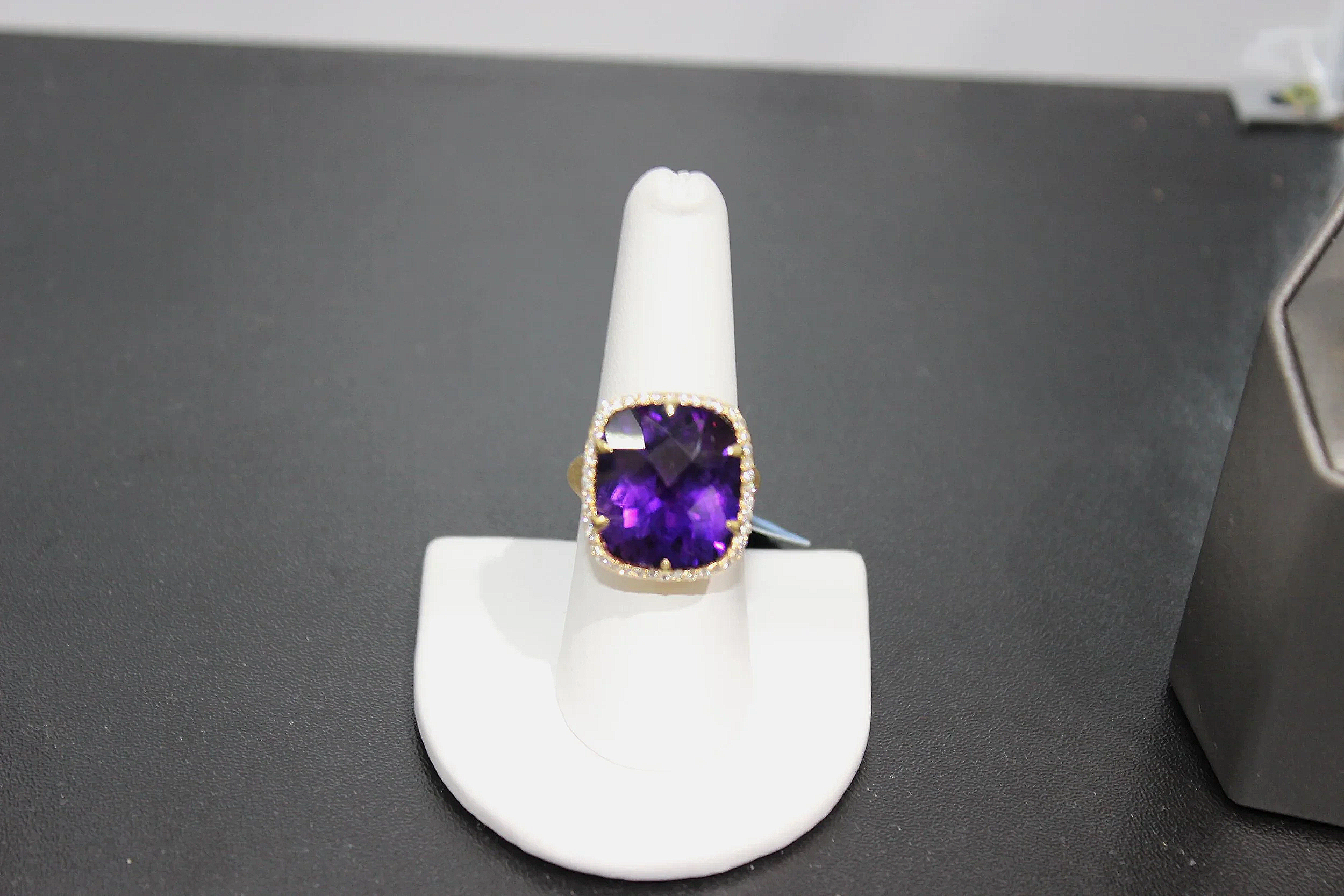 A gold ring with a large, square-cut purple gemstone, set in a jewelry display stand.
