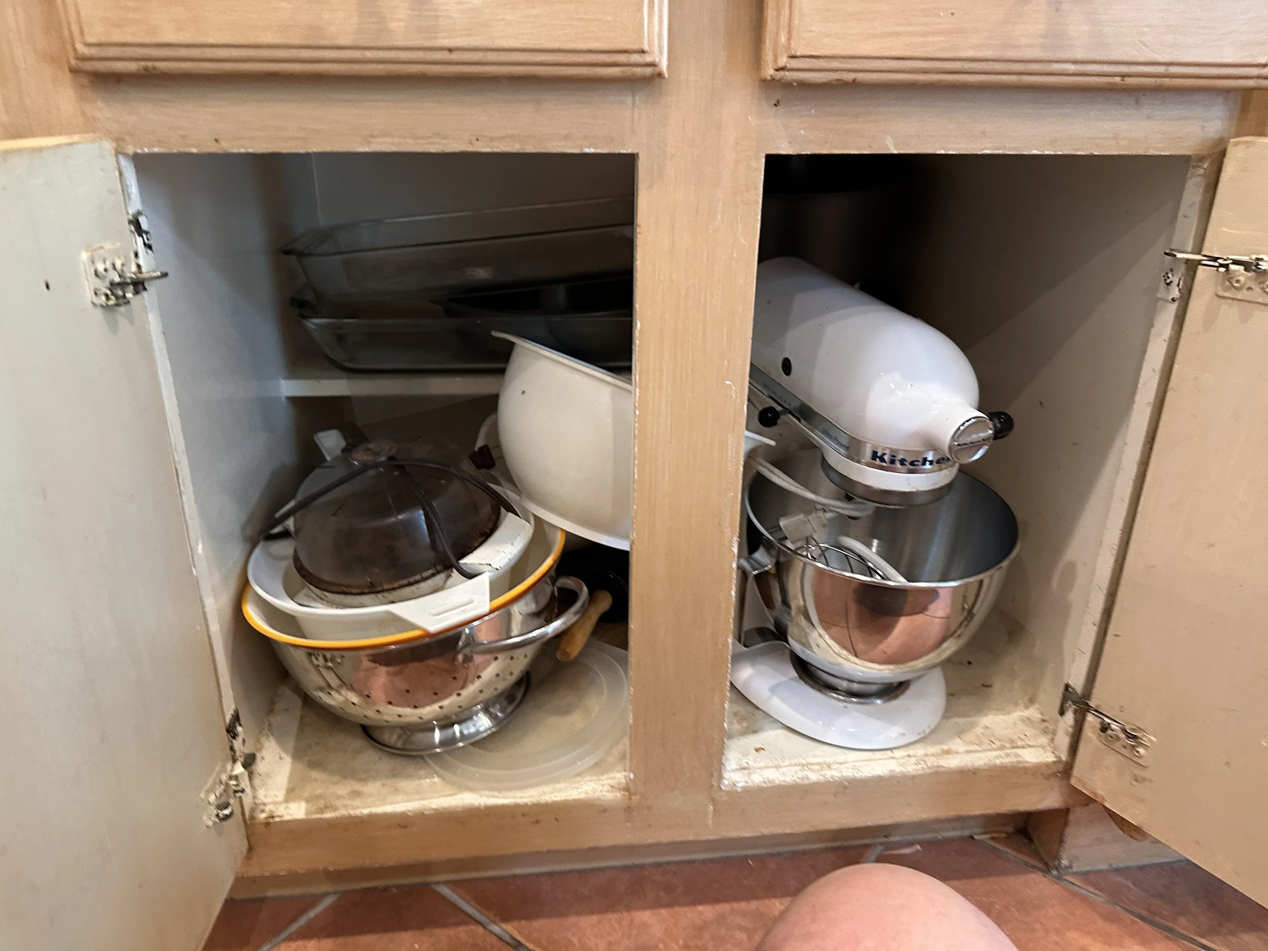 Open kitchen cabinet with various mixing bowls, some stacked and some on shelves, and a stand mixer inside the cabinet.